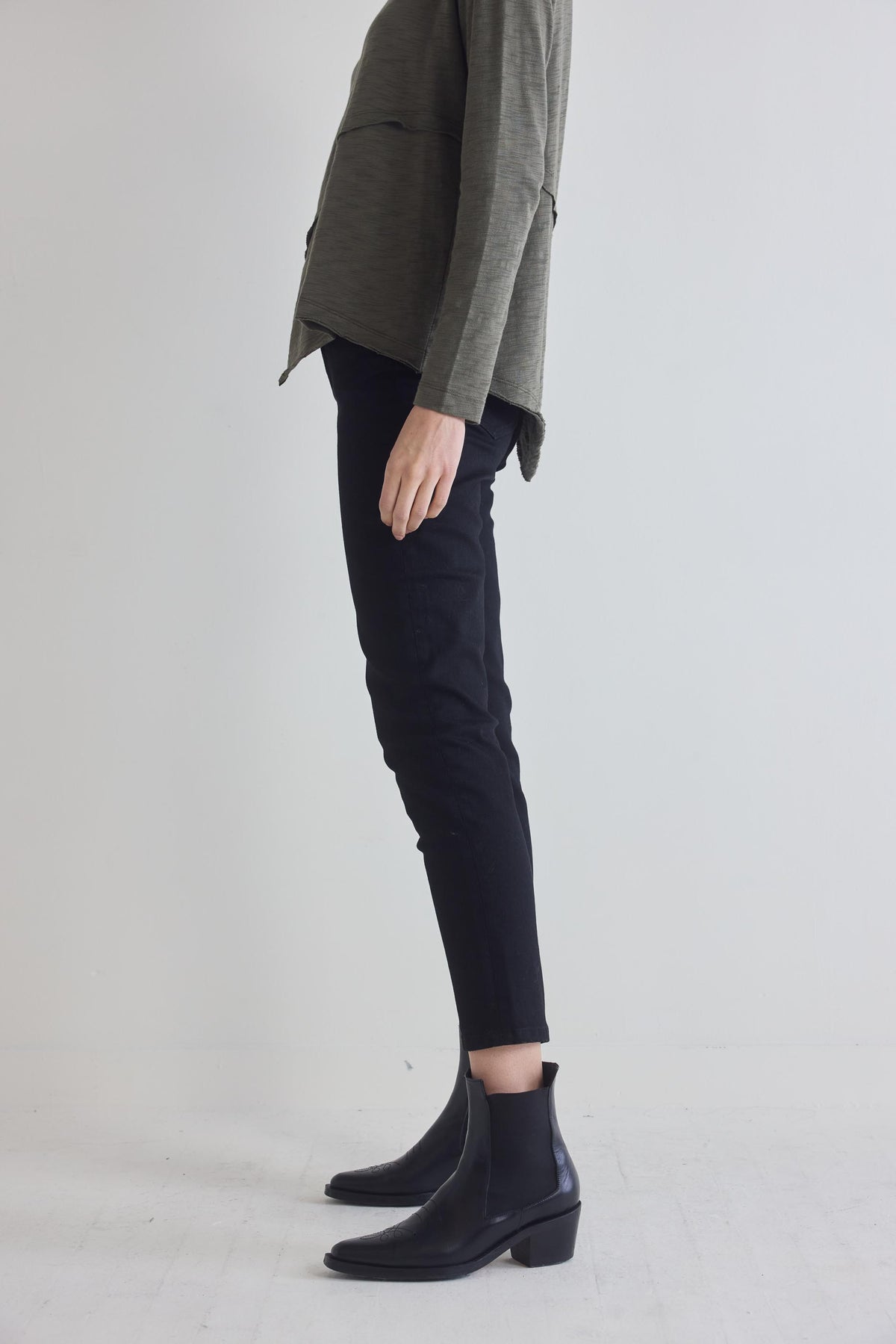 Black fitted jeans with cuffed ankle hem and slim taper, side profile with boots.