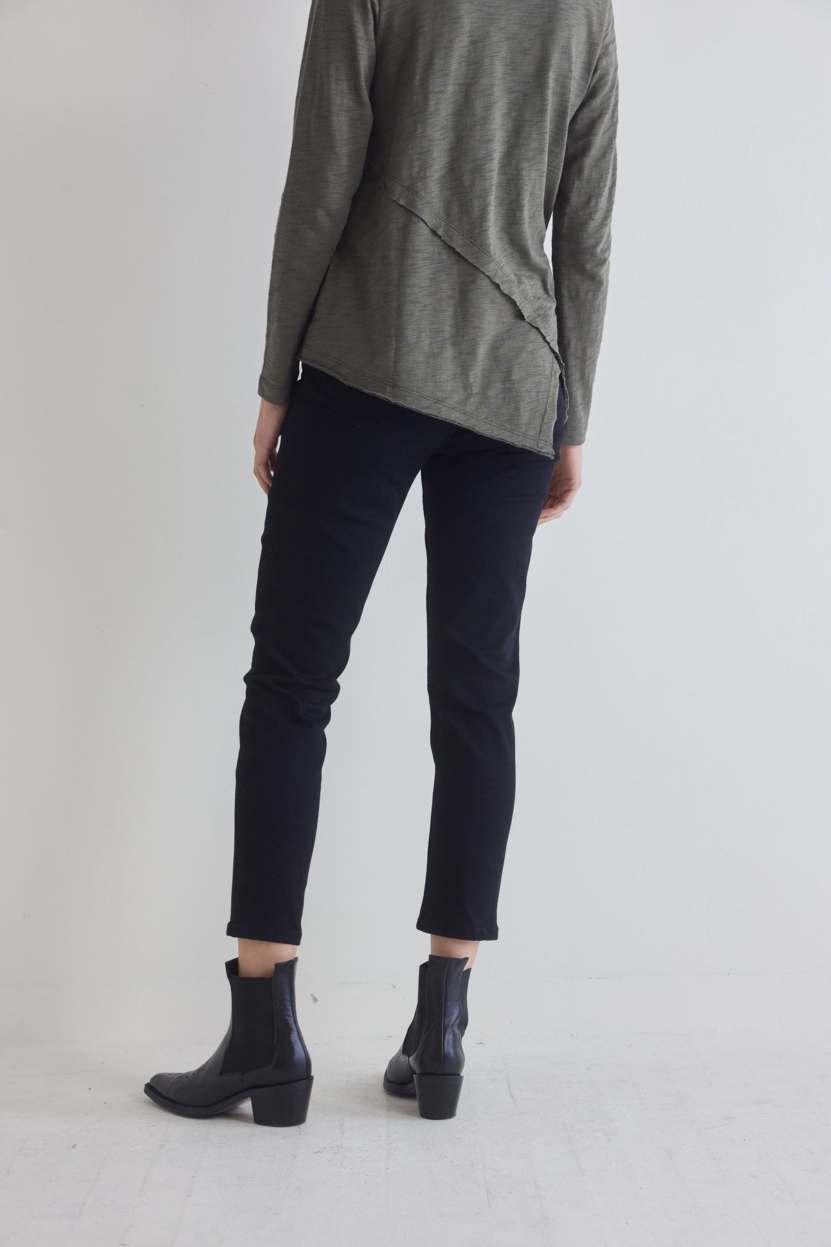 Black fitted jeans showing back yoke and tapered ankle legs, side view with boots.