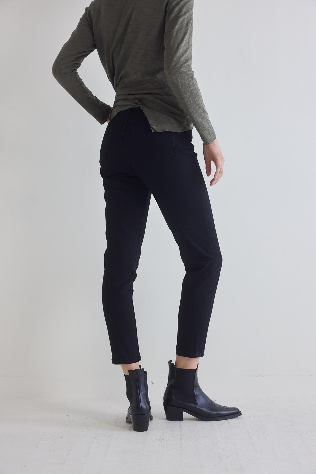 Black fitted jeans with slim tapered legs and ankle hem, side view with boots.