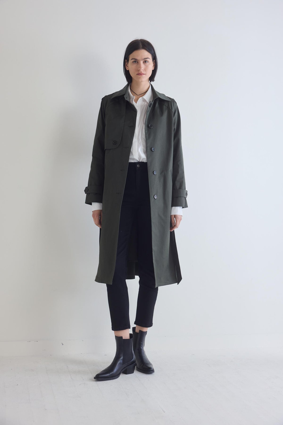 Black fitted jeans, ankle hem and tapered legs, styled under a long dark coat.
