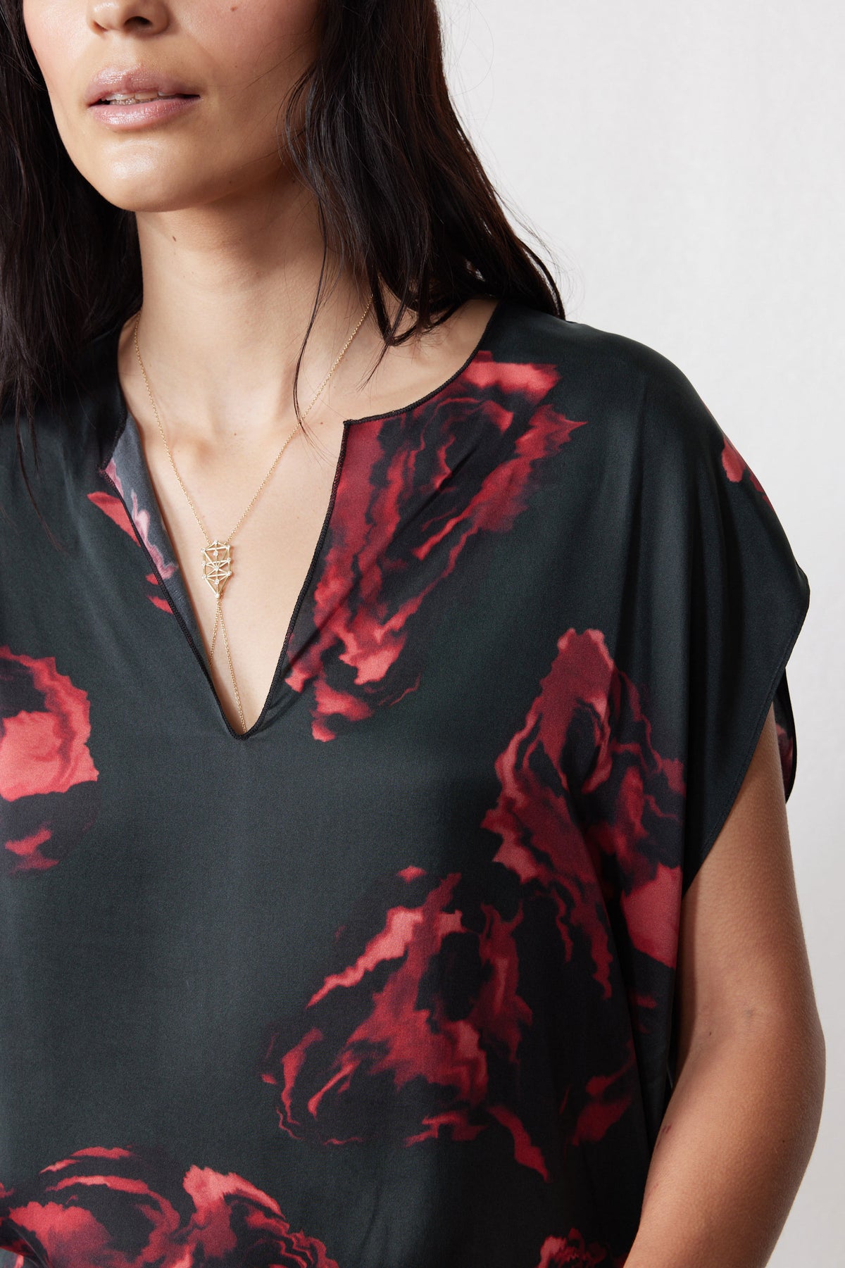 Close-up of rose-print silk top V-neck and shoulder detail in dark with red