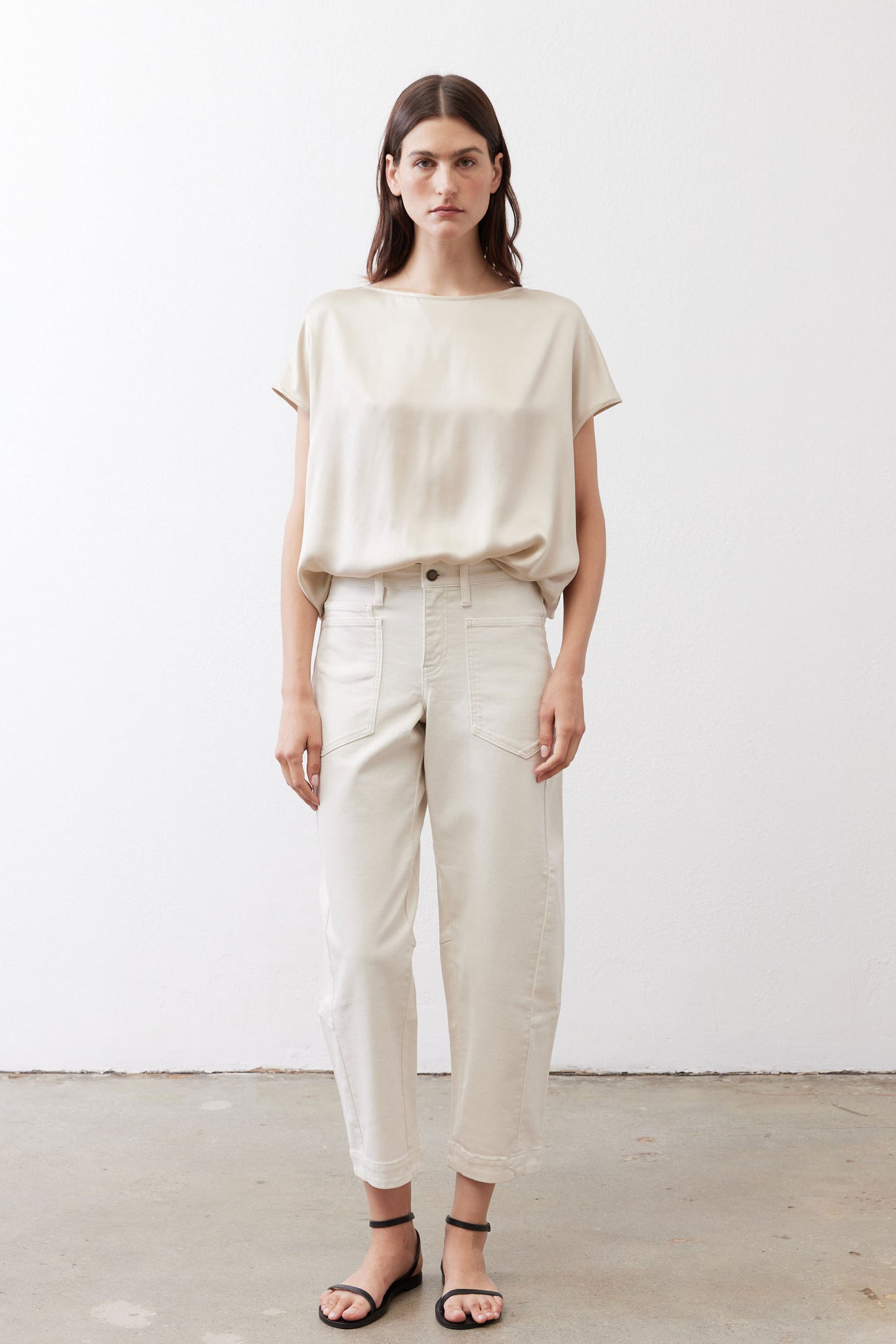 Off-white silk blouse with crew neck and short sleeves, paired with light pants