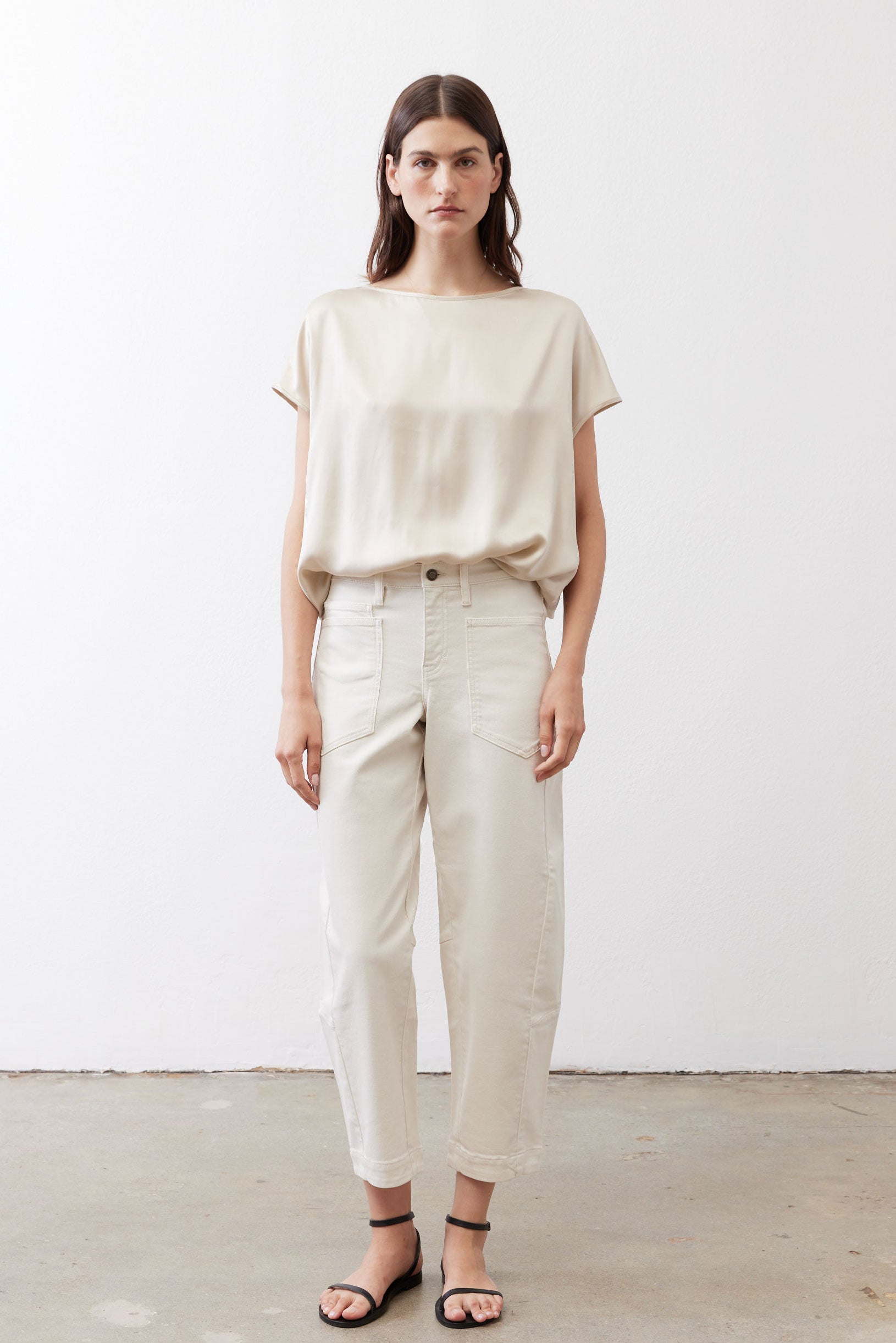 Off-white silk blouse with crew neck and short sleeves, paired with light pants