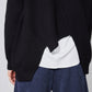 Black asymmetric sweater detail with diagonal seam stitching and white underlayer hem