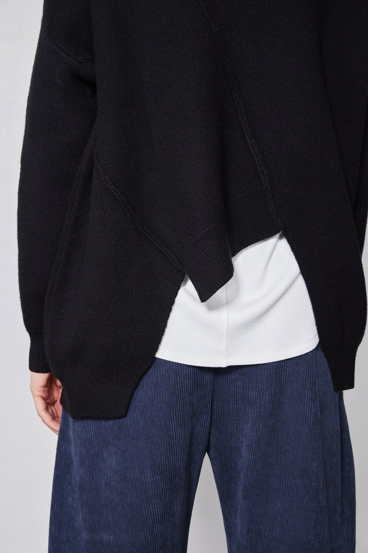 Black asymmetric sweater detail with diagonal seam stitching and white underlayer hem
