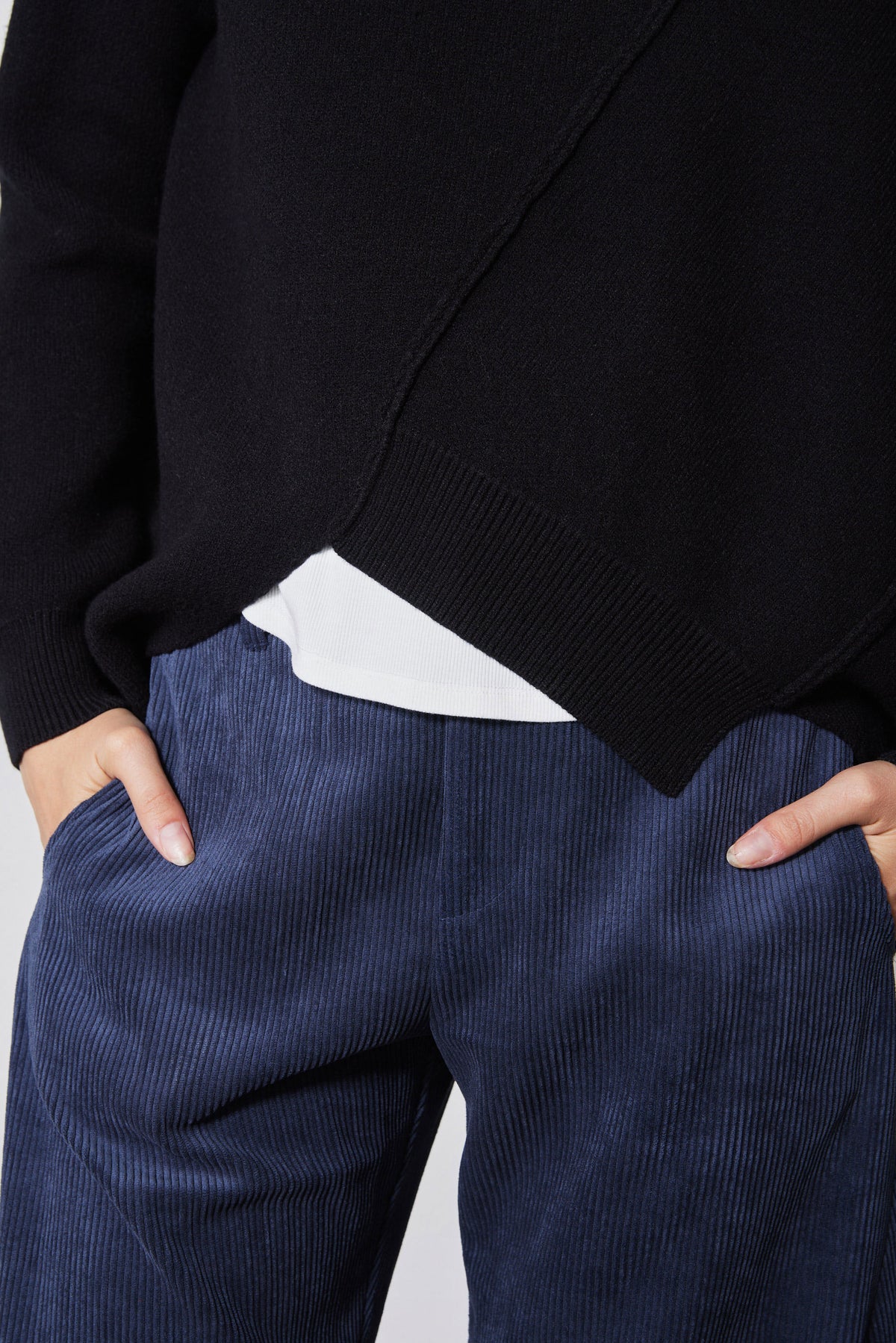 Black sweater hem overlapping white underlayer above blue trousers
