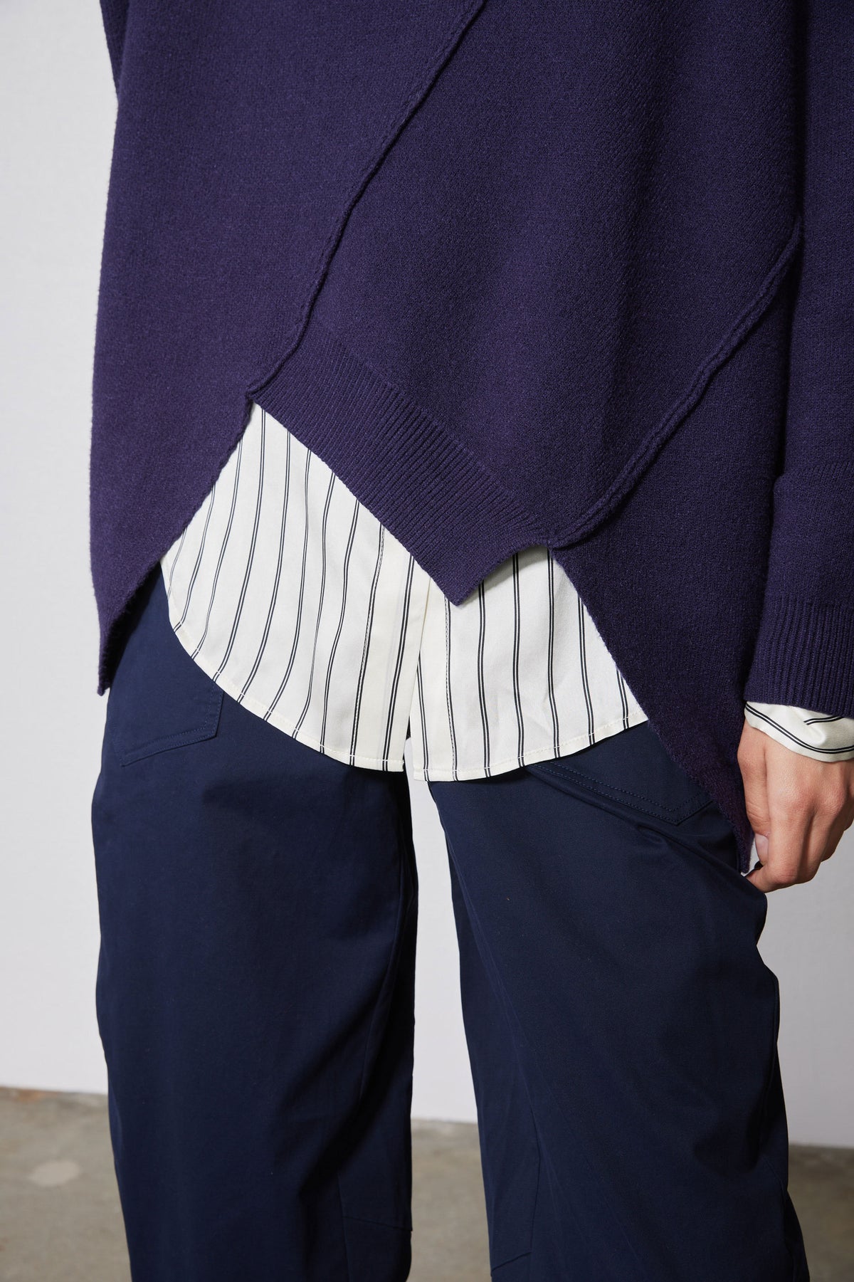 Asymmetric pullover sweater deep purple with diagonal hem opening over a striped shirt