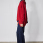 Red asymmetric pullover sweater shown from side; crew neck and ribbed cuffs