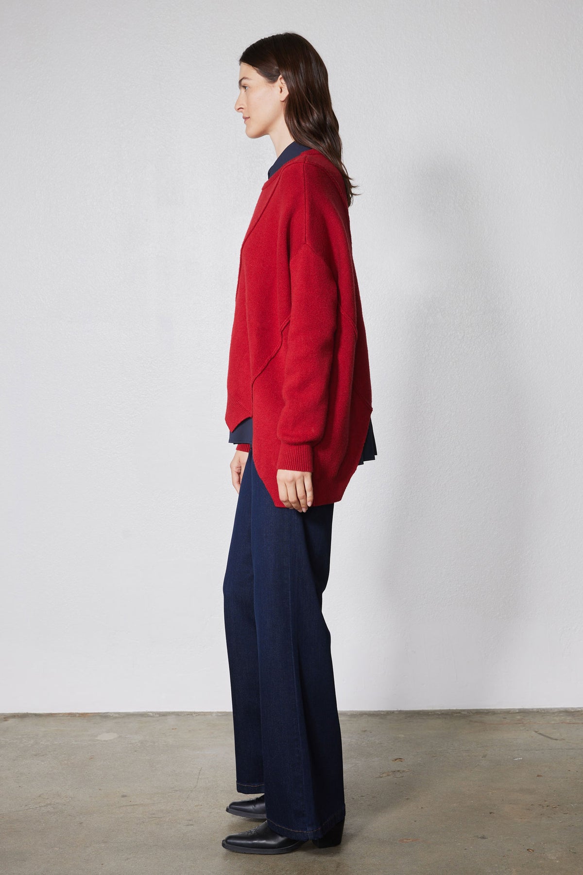 Red asymmetric pullover sweater shown from side; crew neck and ribbed cuffs