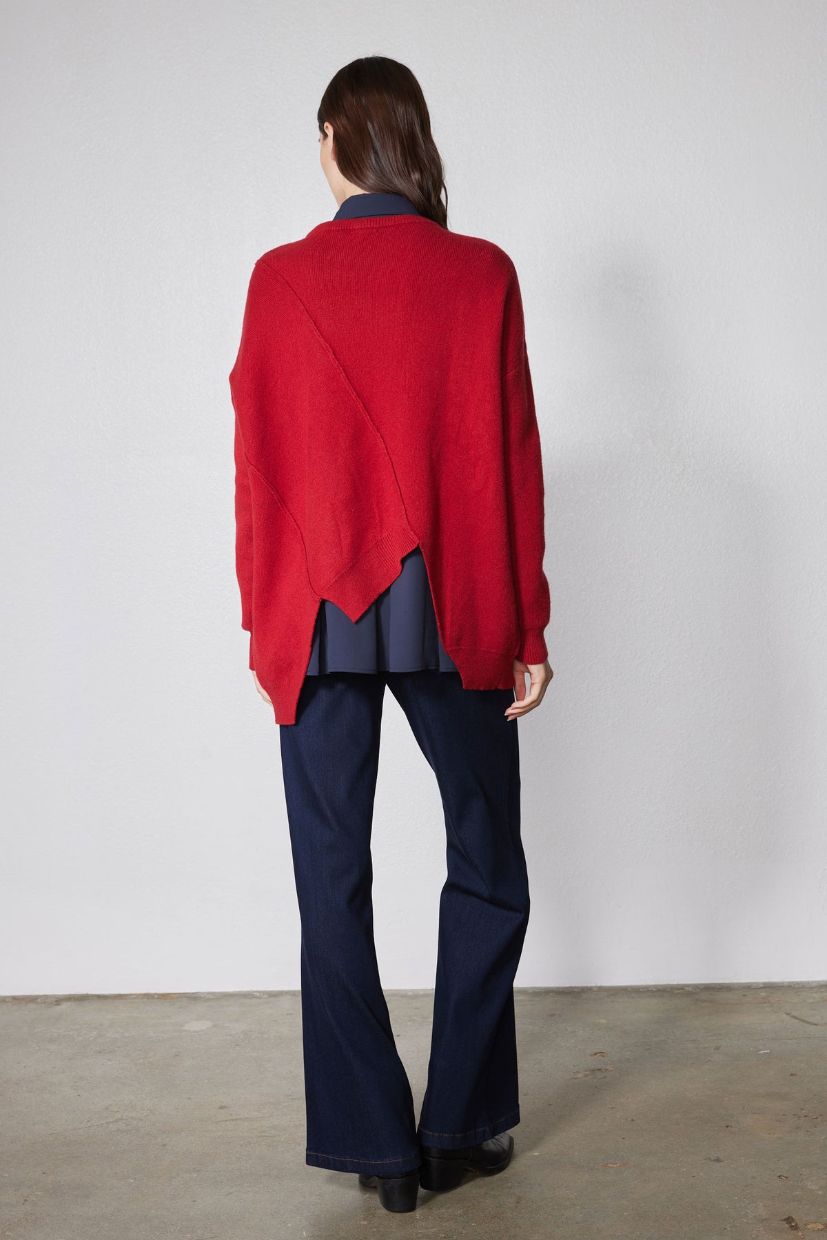 Back view of red asymmetric pullover sweater with angled seam across shoulders