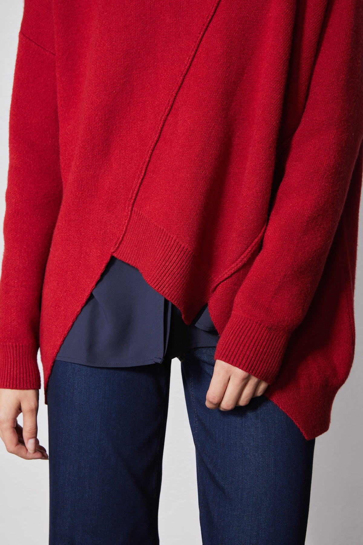 Red asymmetric pullover sweater close-up; ribbed cuffs and angled hem panel