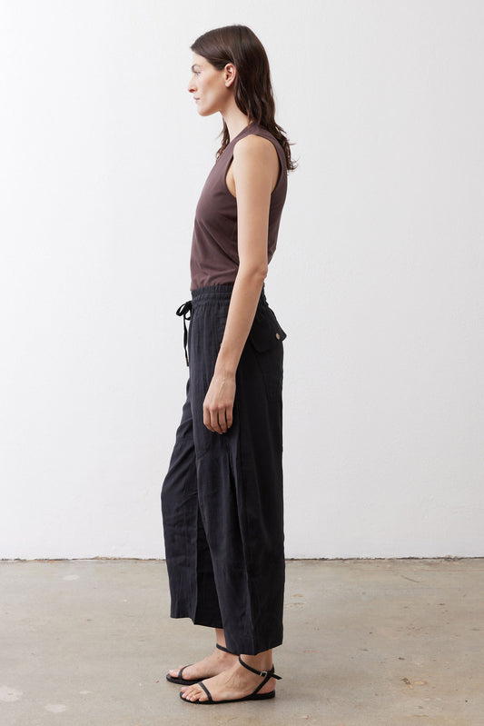 Black baggy utility pants in side profile with elastic waist, drawstring ties, wide legs
