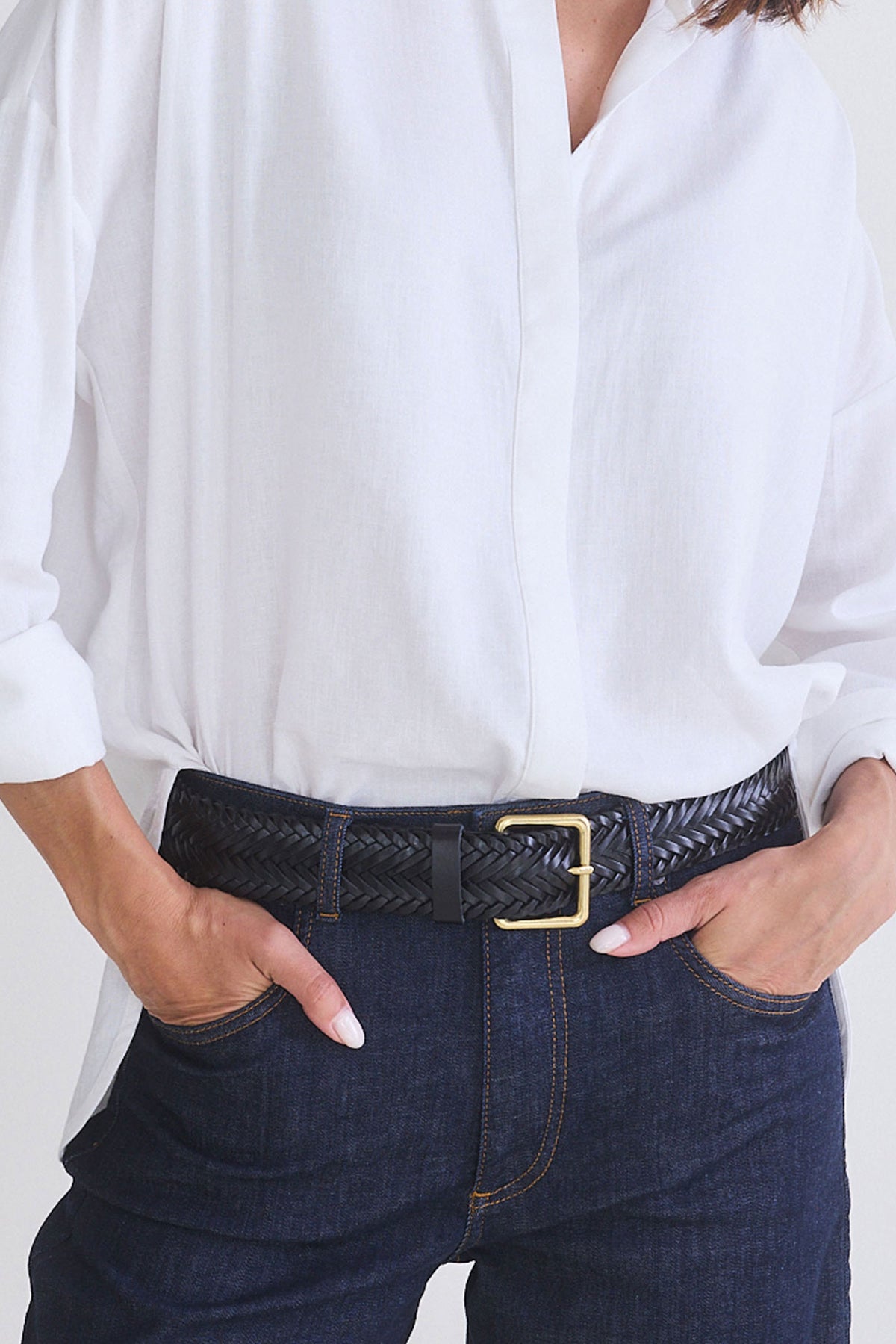 Black textured woven leather belt with gold buckle worn on dark jeans