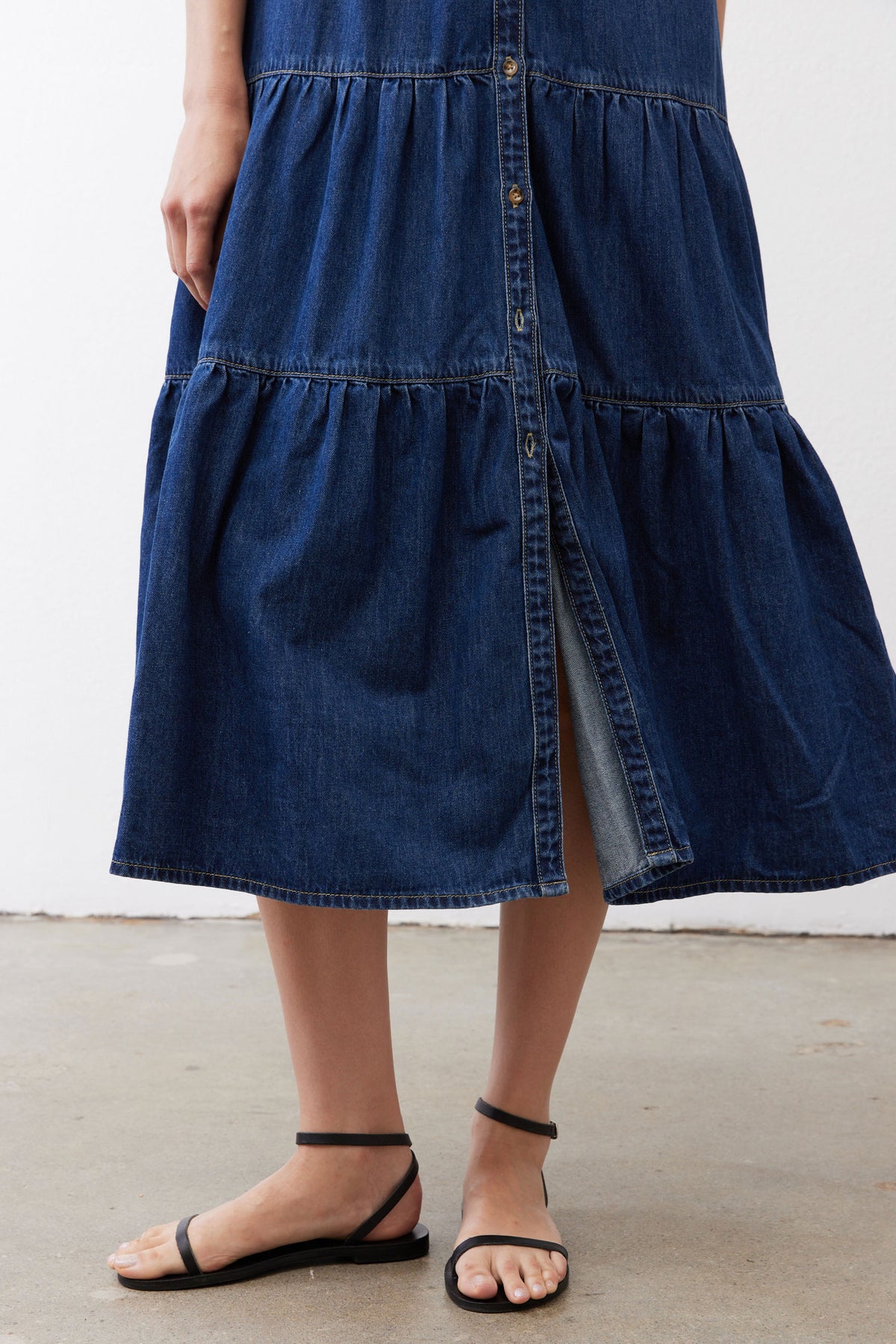 Medium-wash denim midi dress hem with tiered panels and center button detail