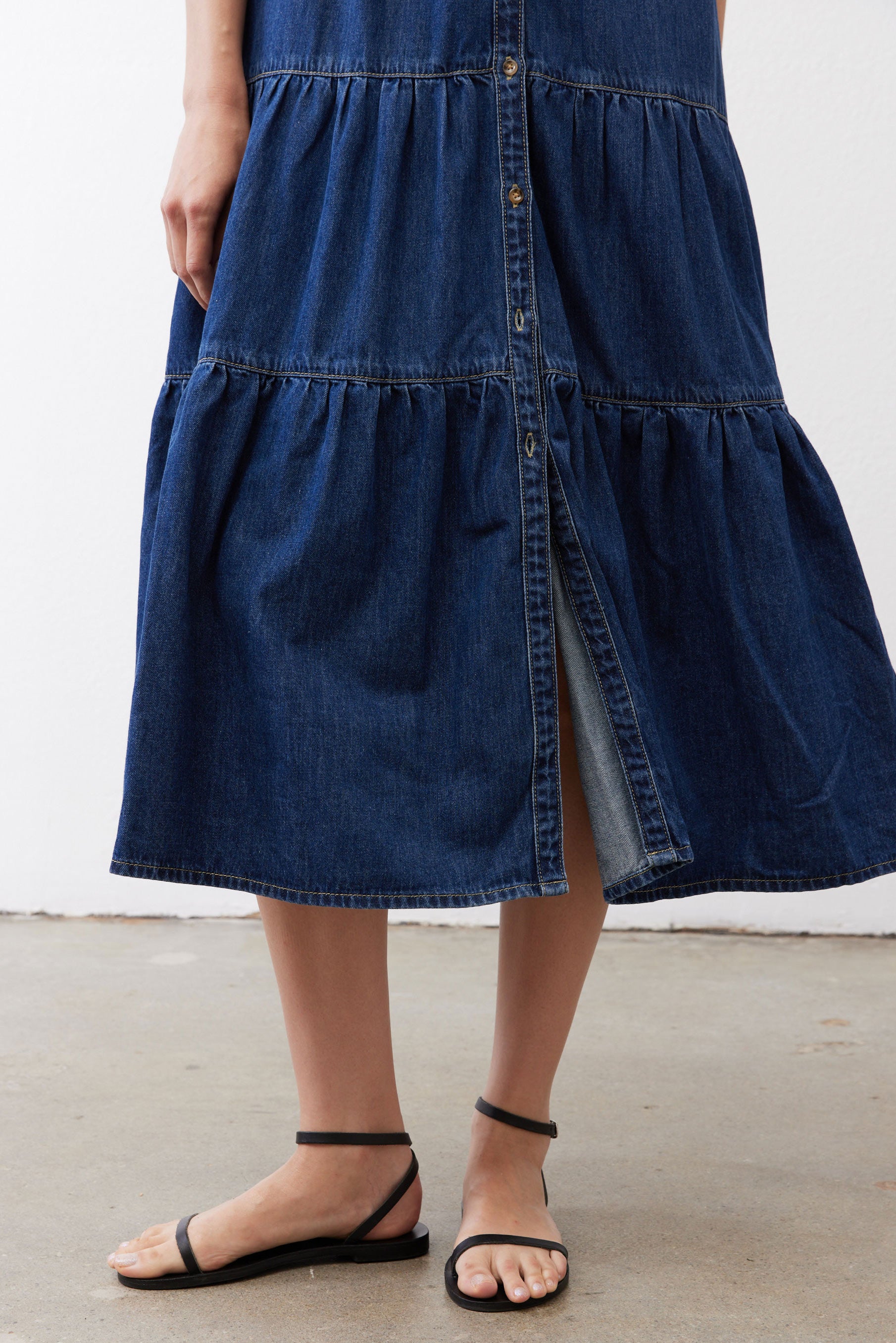Medium-wash denim midi dress hem with tiered panels and center button detail