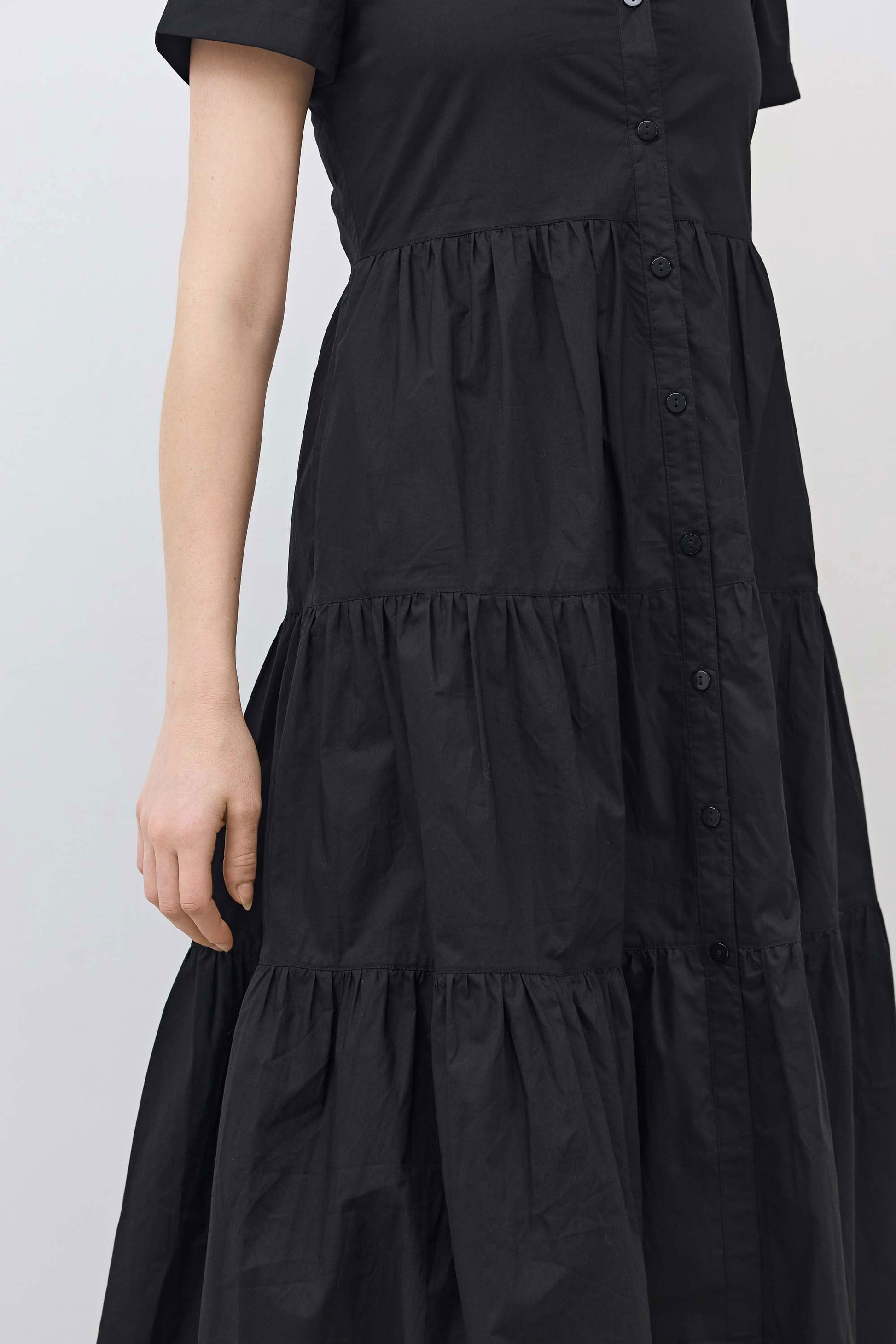 Close-up of black tiered poplin dress with button placket and gathered skirt