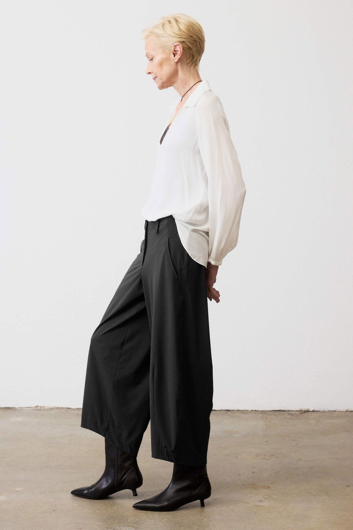 Black wide-leg pants, side view, elastic waistband and deep front pockets.