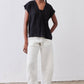 Black cinched-neck poplin top with short sleeves, worn with light-colored trousers