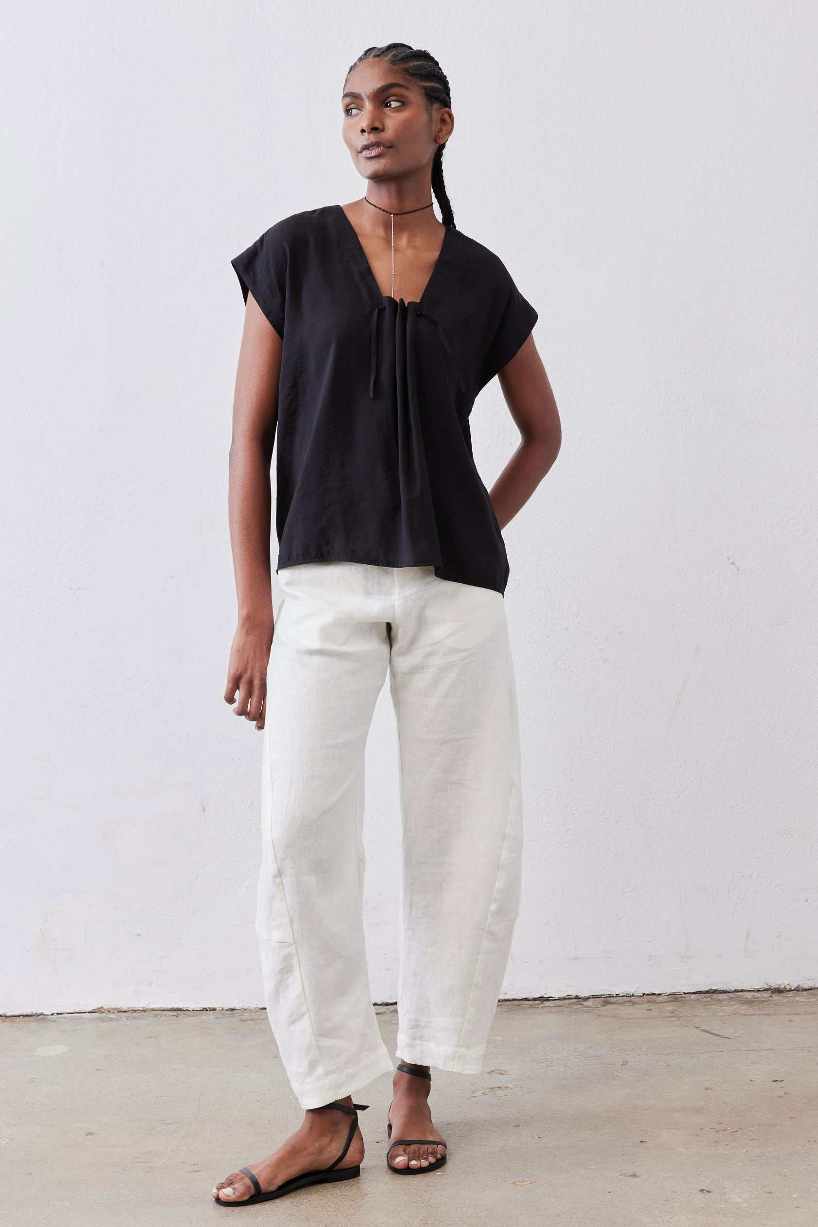Black cinched-neck poplin top with short sleeves, worn with light-colored trousers