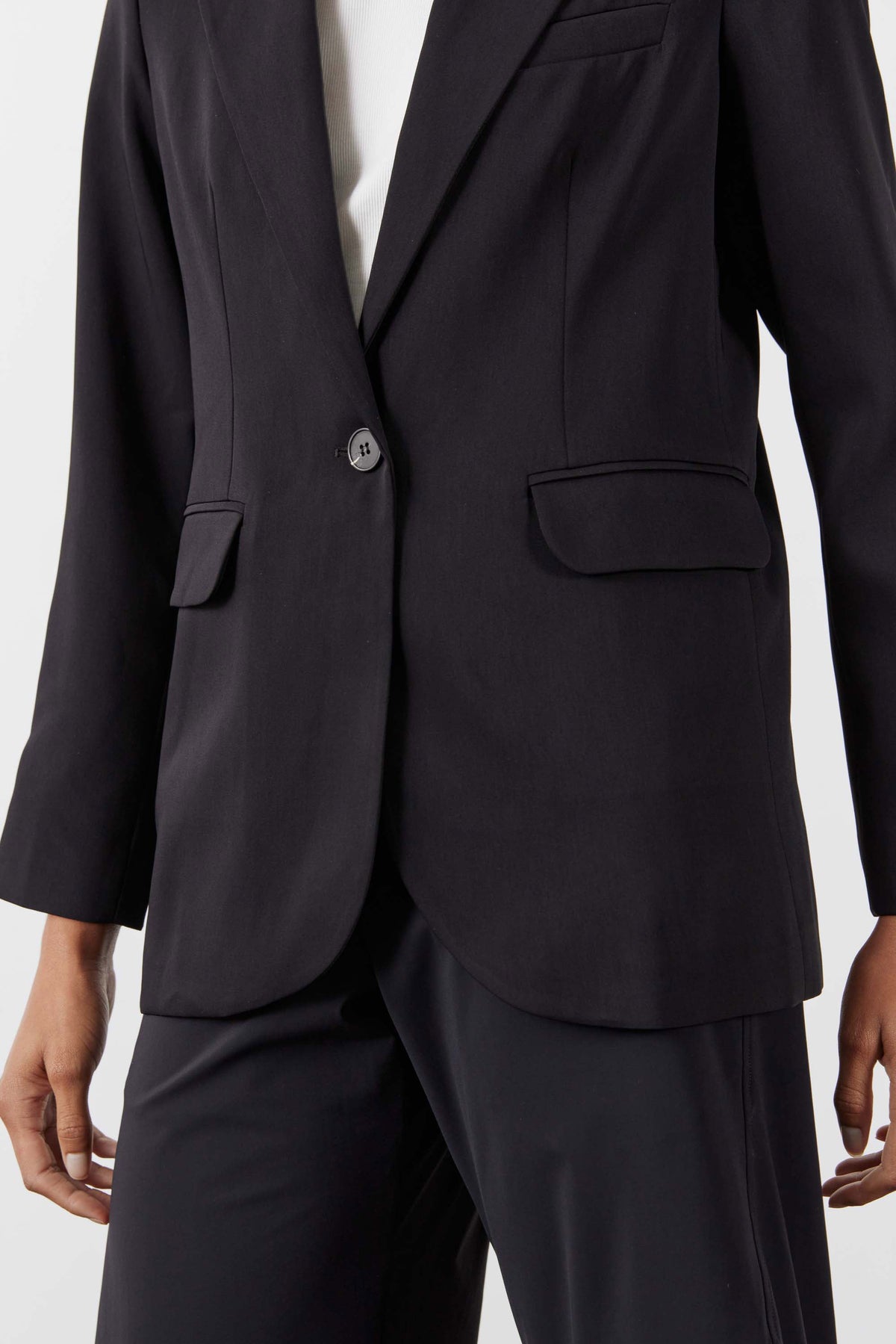 Black blazer front close-up with single button, flap pockets, and welt sleeve