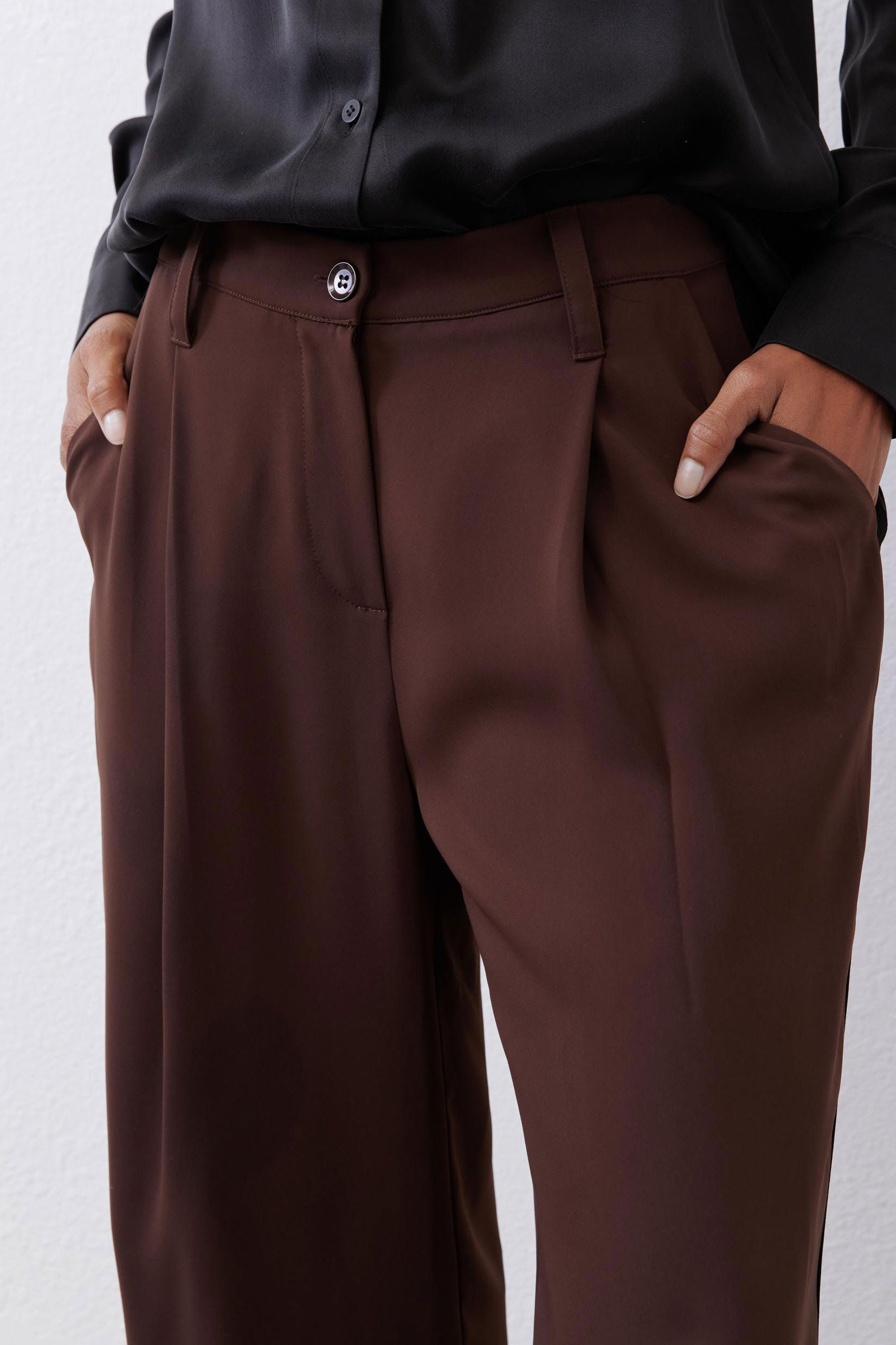 Close-up of dark brown button-front wide-leg pants with belt loops and side seam