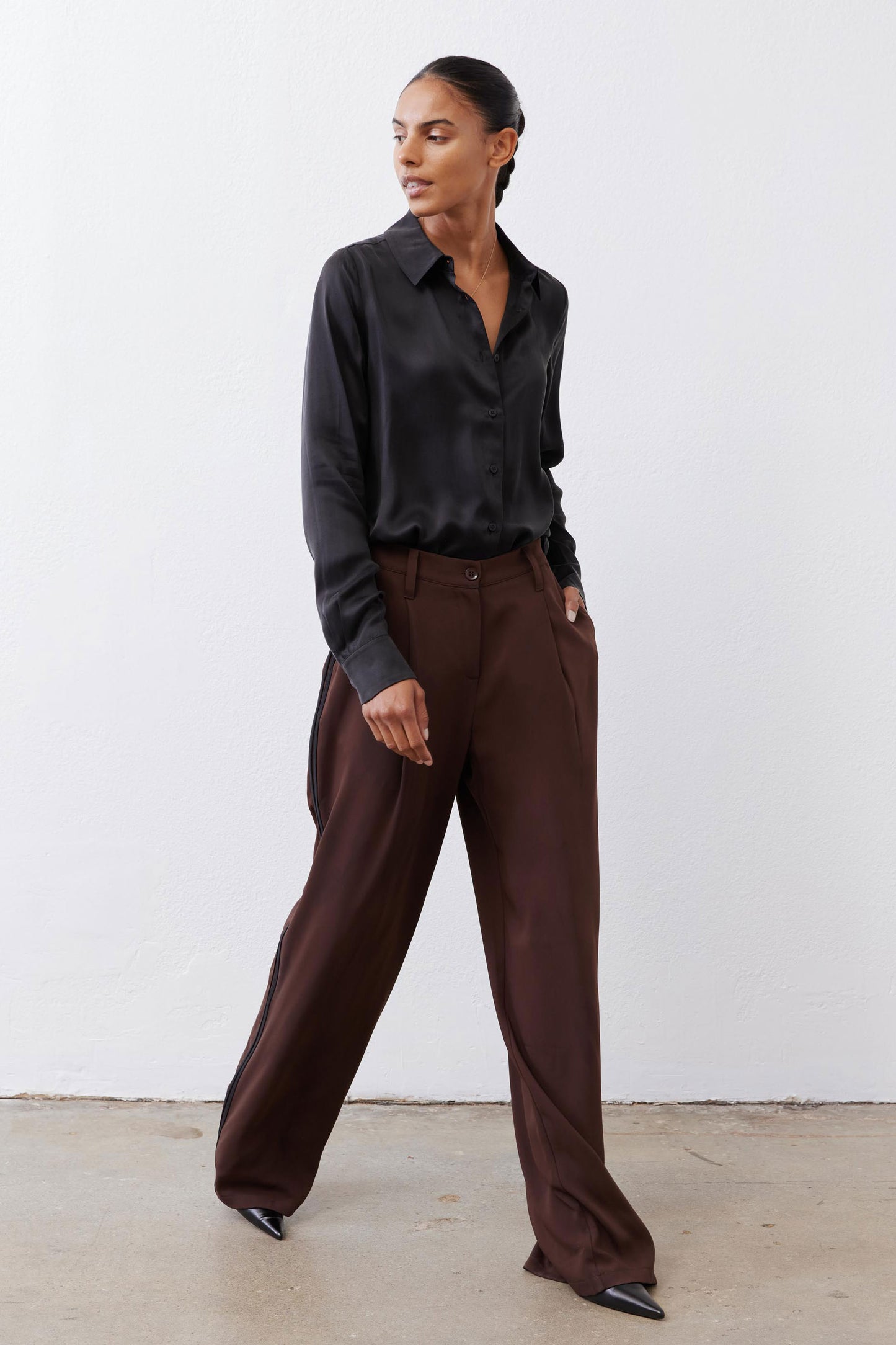 Dark brown wide-leg pleated trousers with black side stripe and button closure