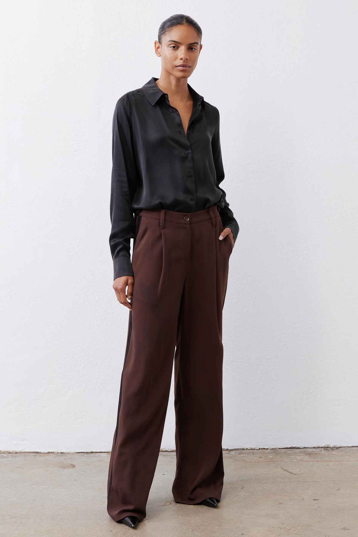 Brown wide-leg trousers with pleats, button front, and subtle black side stripe