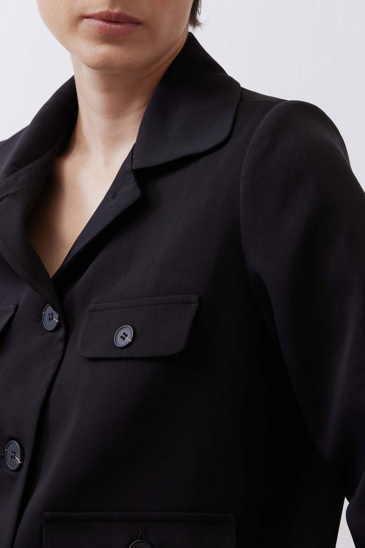 Black collared classic jacket close-up of chest pockets and round button detail