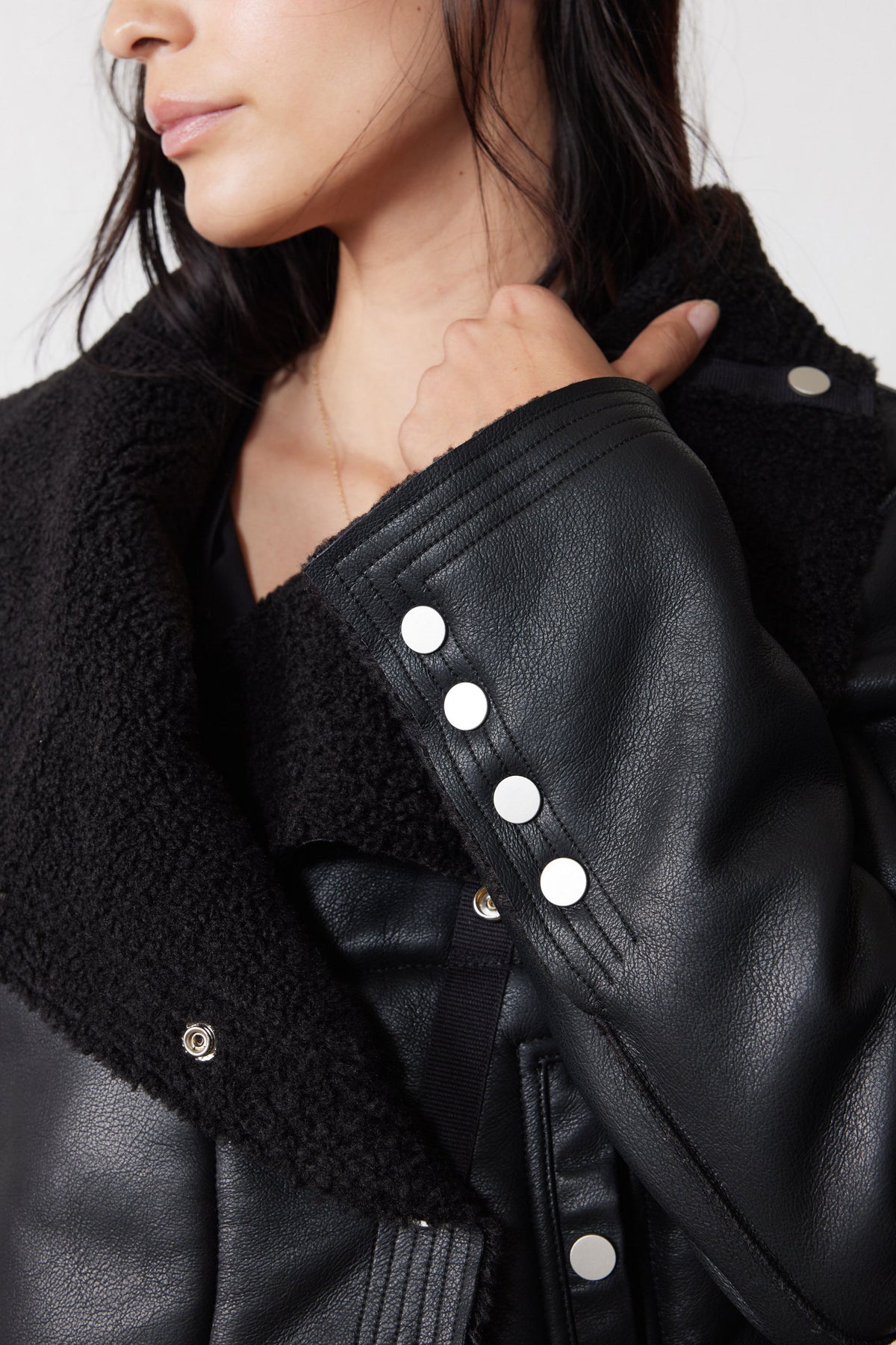 Black moto jacket detail showing plush shearling lapel and snap-button cuff
