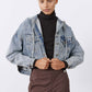 Washed-blue denim jacket with hood and button front, model holding collar