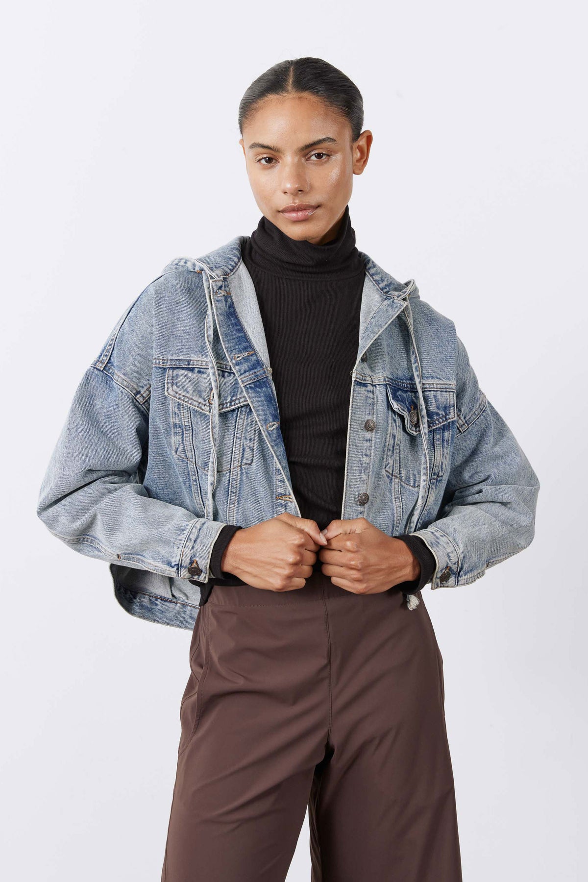 Washed-blue denim jacket with hood and button front, model holding collar