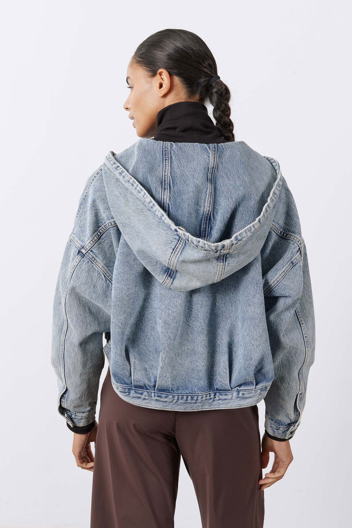 Washed-blue hooded denim jacket with drawstring, back view over brown pants
