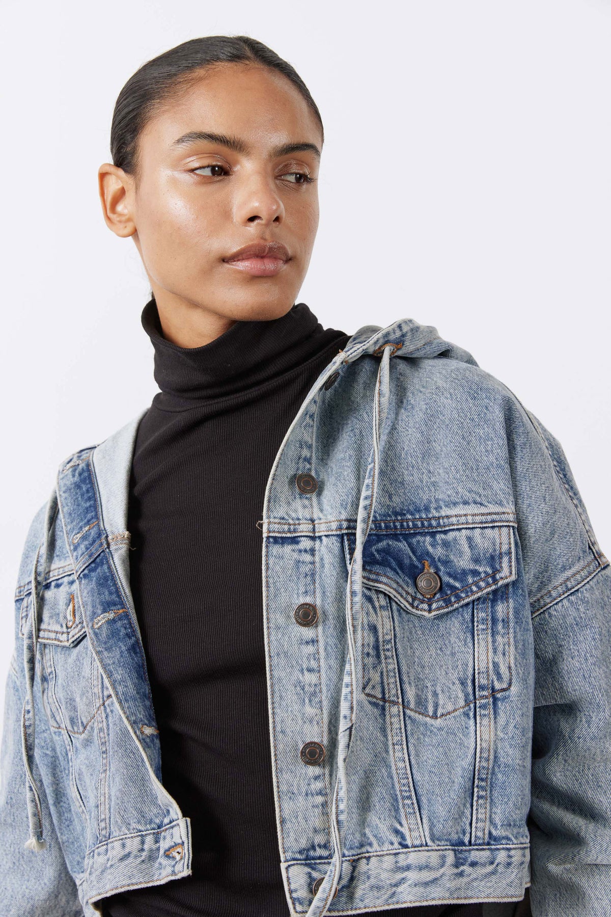 Washed-blue denim jacket with hood and buttoned chest, worn over black turtleneck