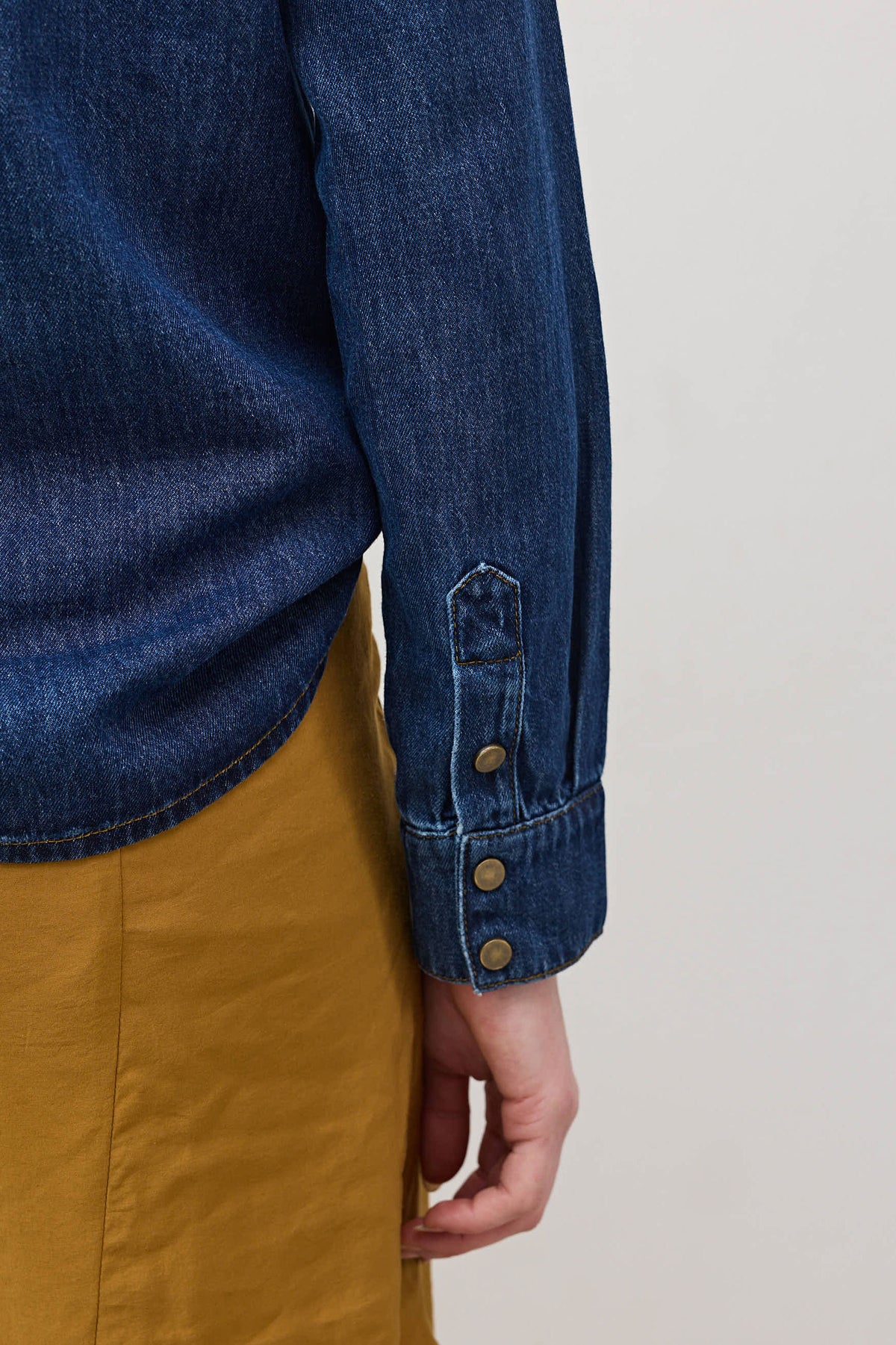 Medium-wash denim shirt cuff with buttoned placket and sleeve seam detail