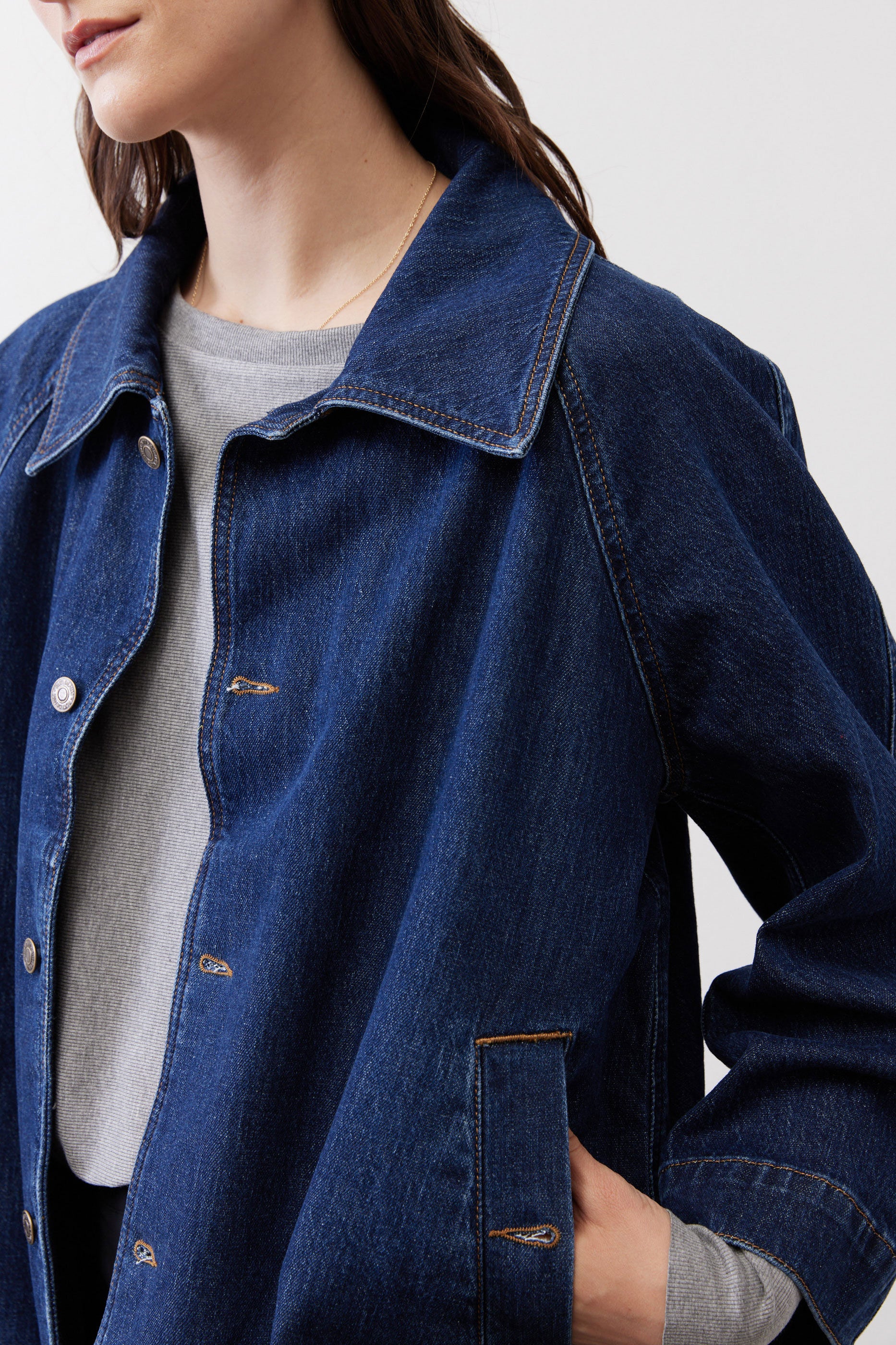 Denim cropped swing jacket close-up: buttoned collar, chest pocket, and visible stitching