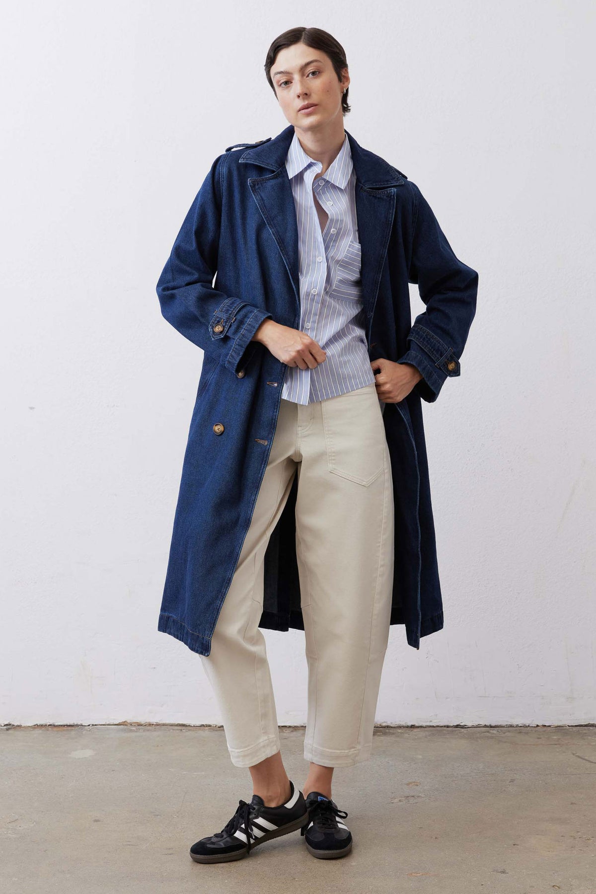Dark wash denim trench coat with buttoned cuffs and belted waist