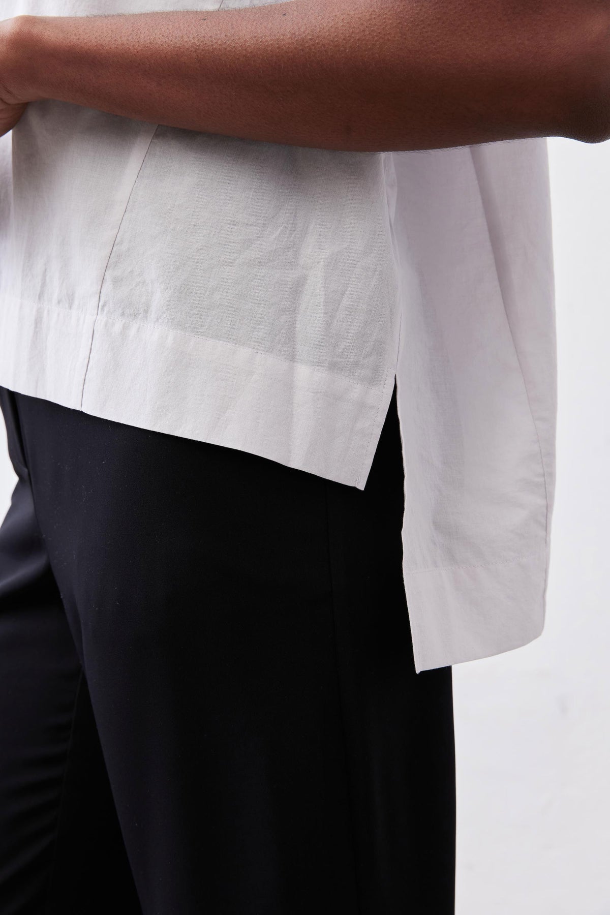 White dolman drape-neck top hem detail over black pants