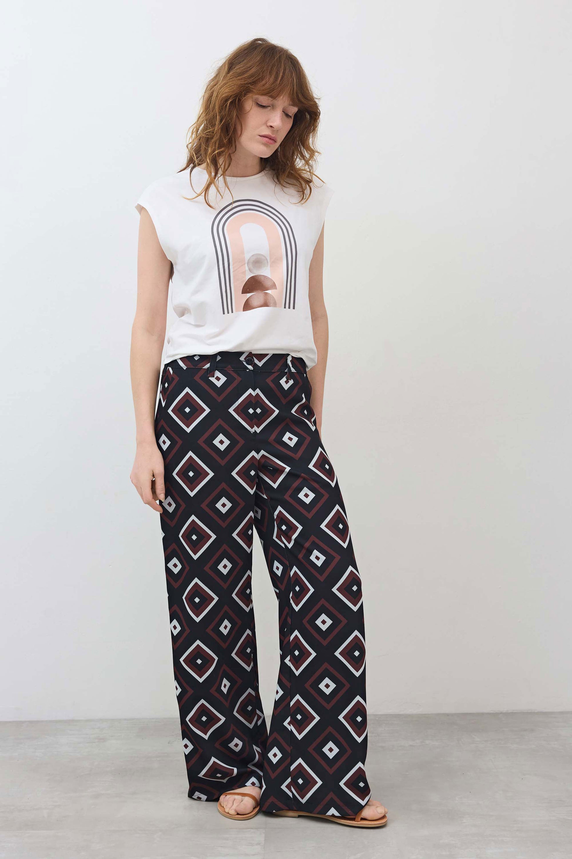 White sleeveless graphic tee with centered rainbow arch print and curved hem