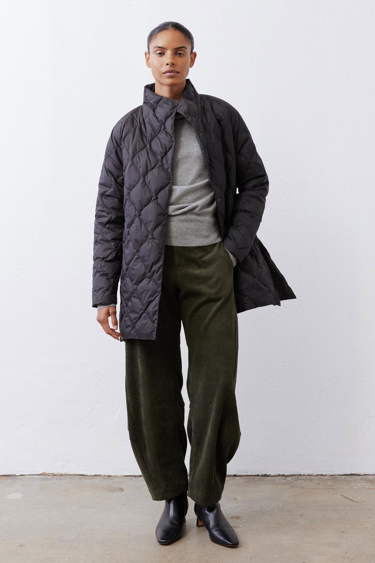 Black long down puffer coat with diamond quilting and snap-button front.