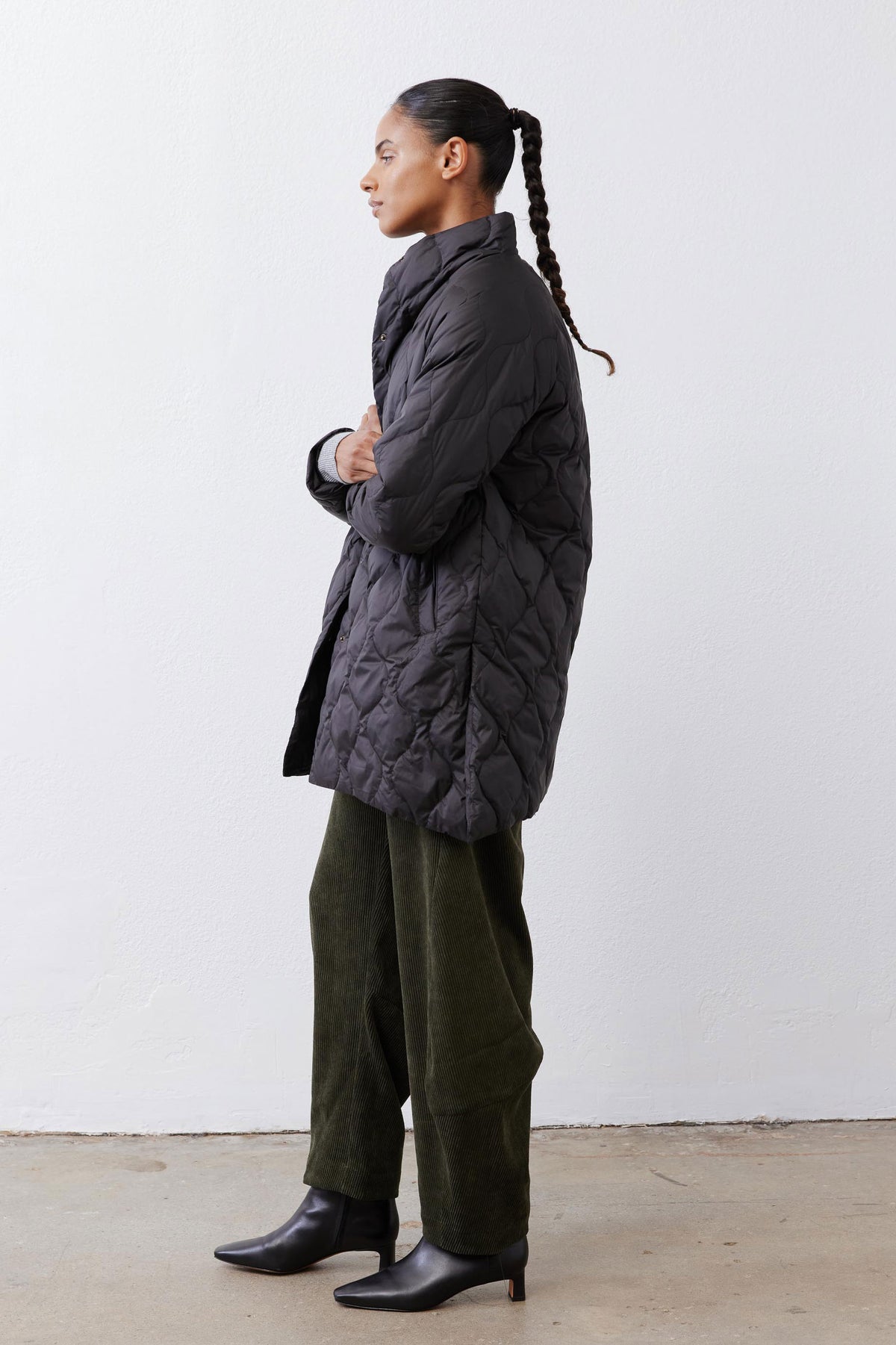 Black long down puffer coat in side profile with diamond quilting and snap front.