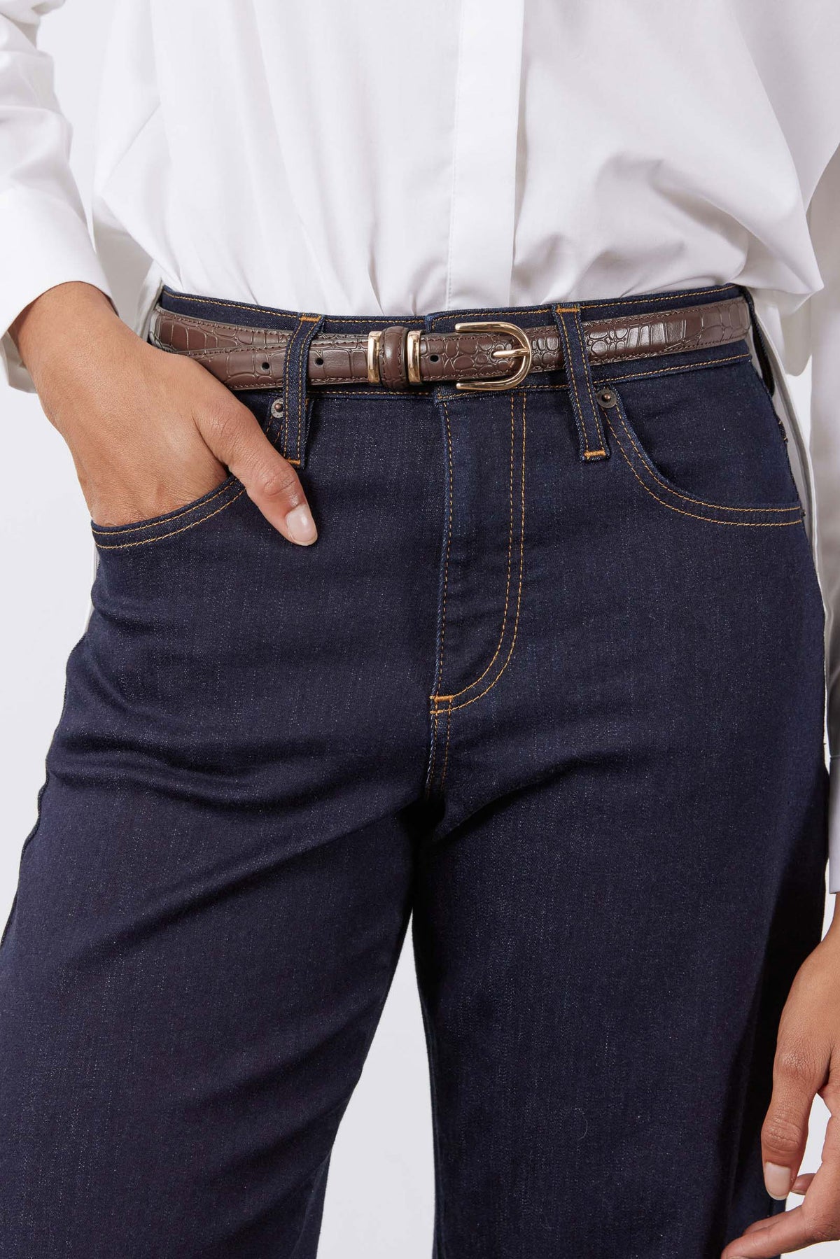 Chocolate croc-embossed belt with oval buckle on dark denim jeans at waist