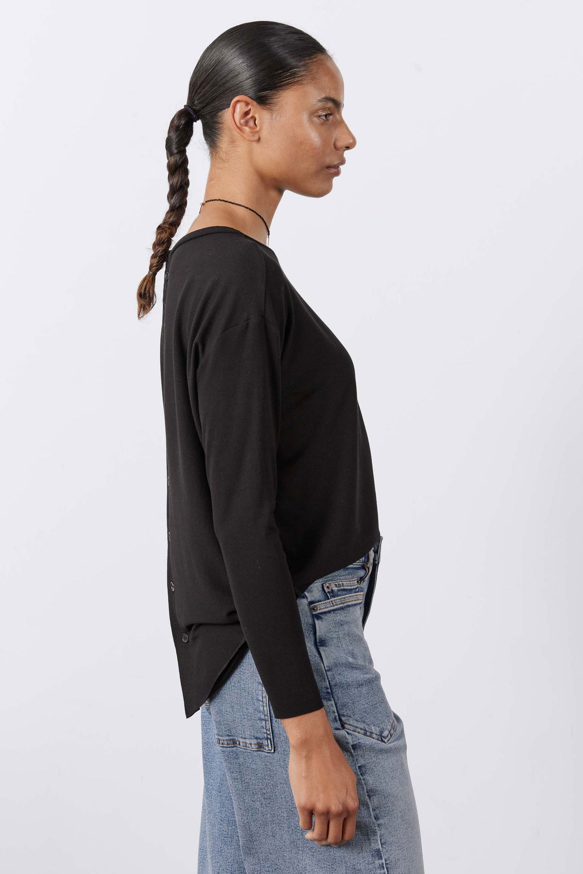 Black long-sleeve top side view with back button detail and curved hem