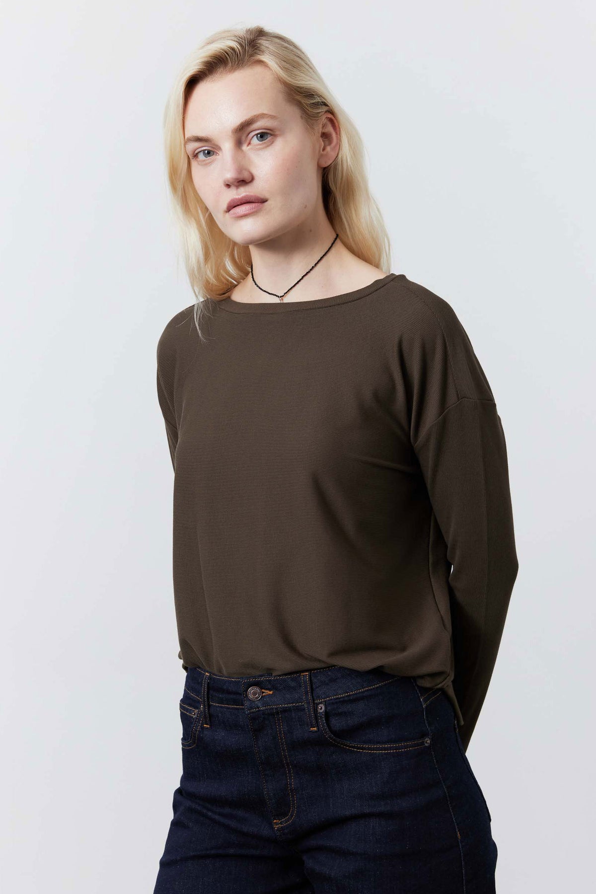 Dark taupe long-sleeve crewneck top, simple neckline, worn with jeans, angled view
