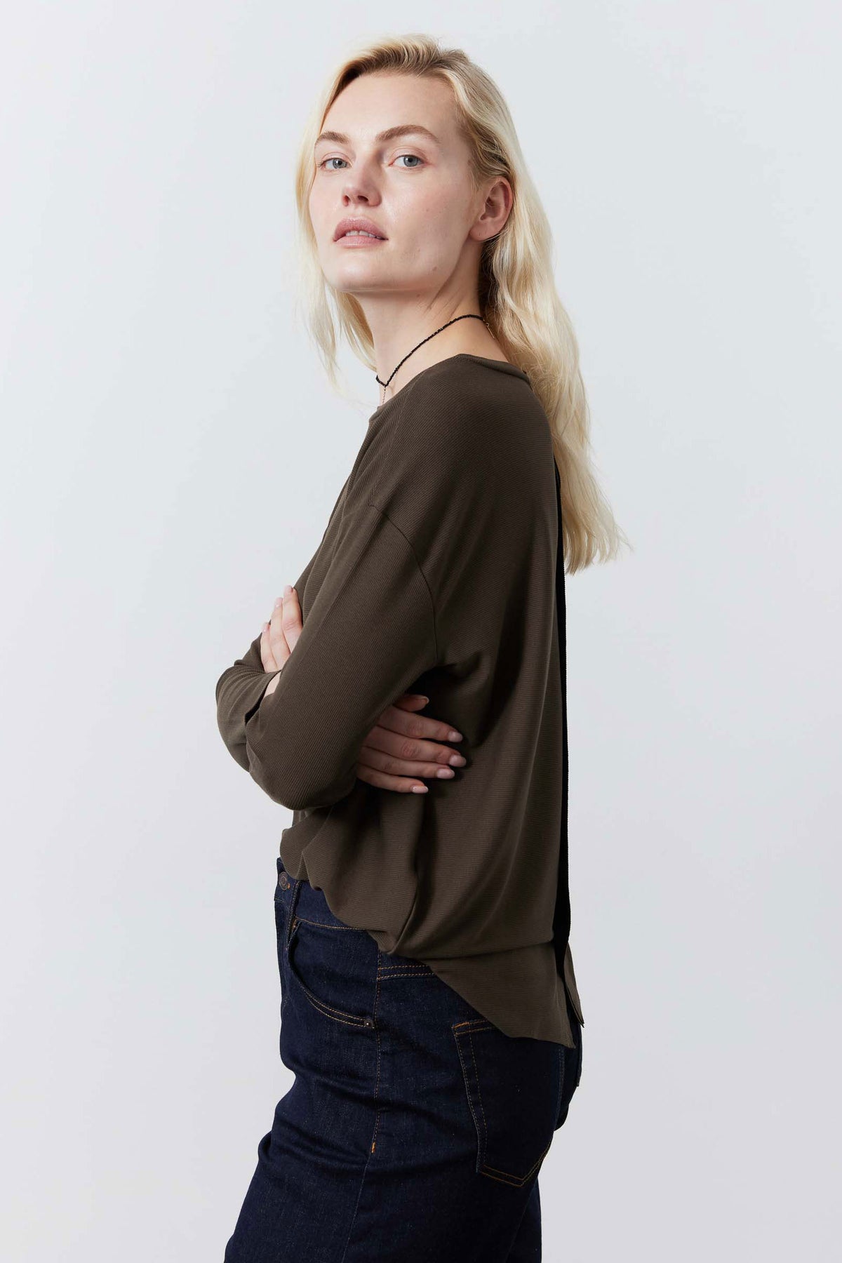 Dark taupe long-sleeve crewneck top, side profile view, worn with jeans