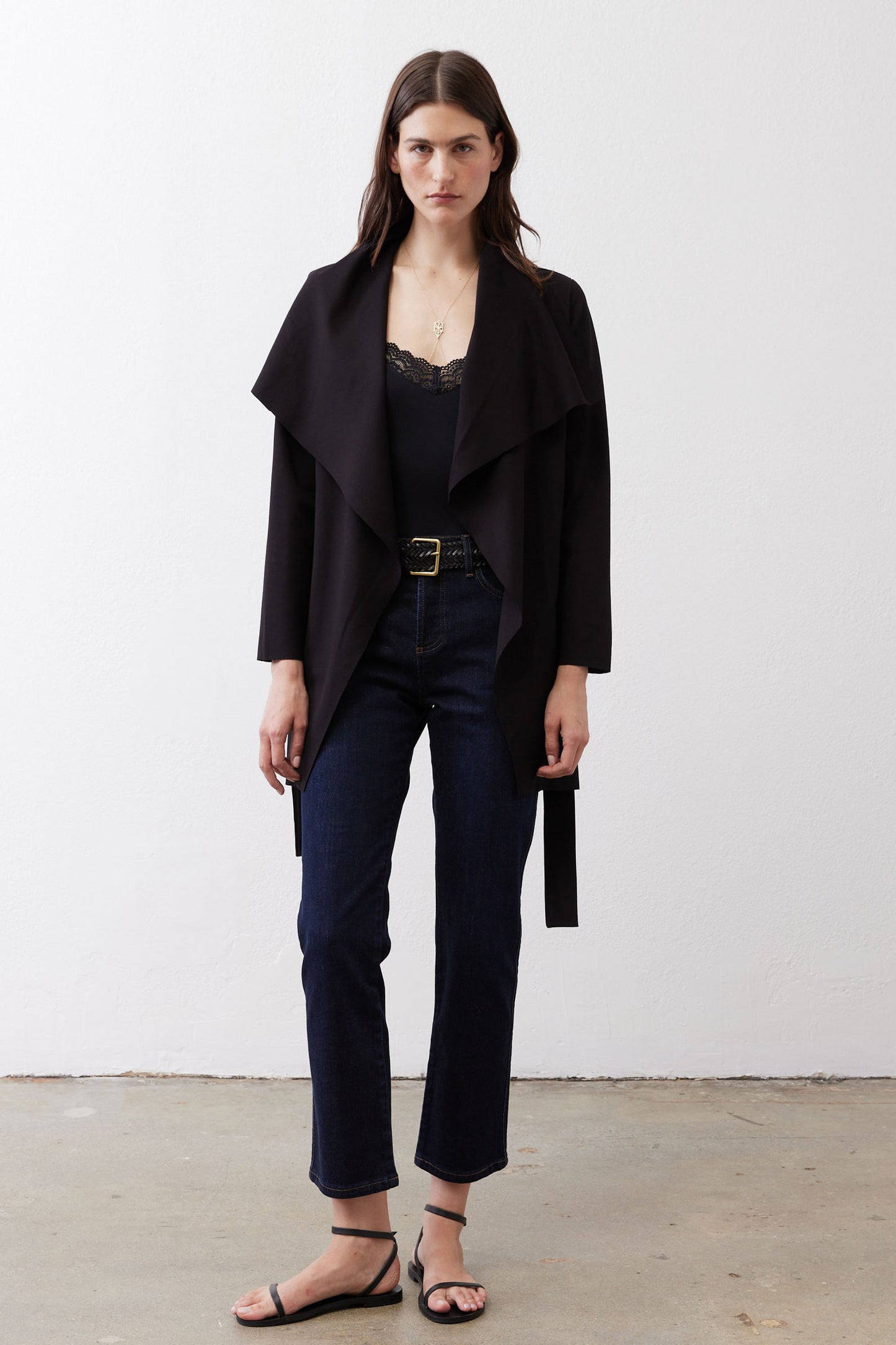 Black draped jacket with tie belt over dark jeans, open front.