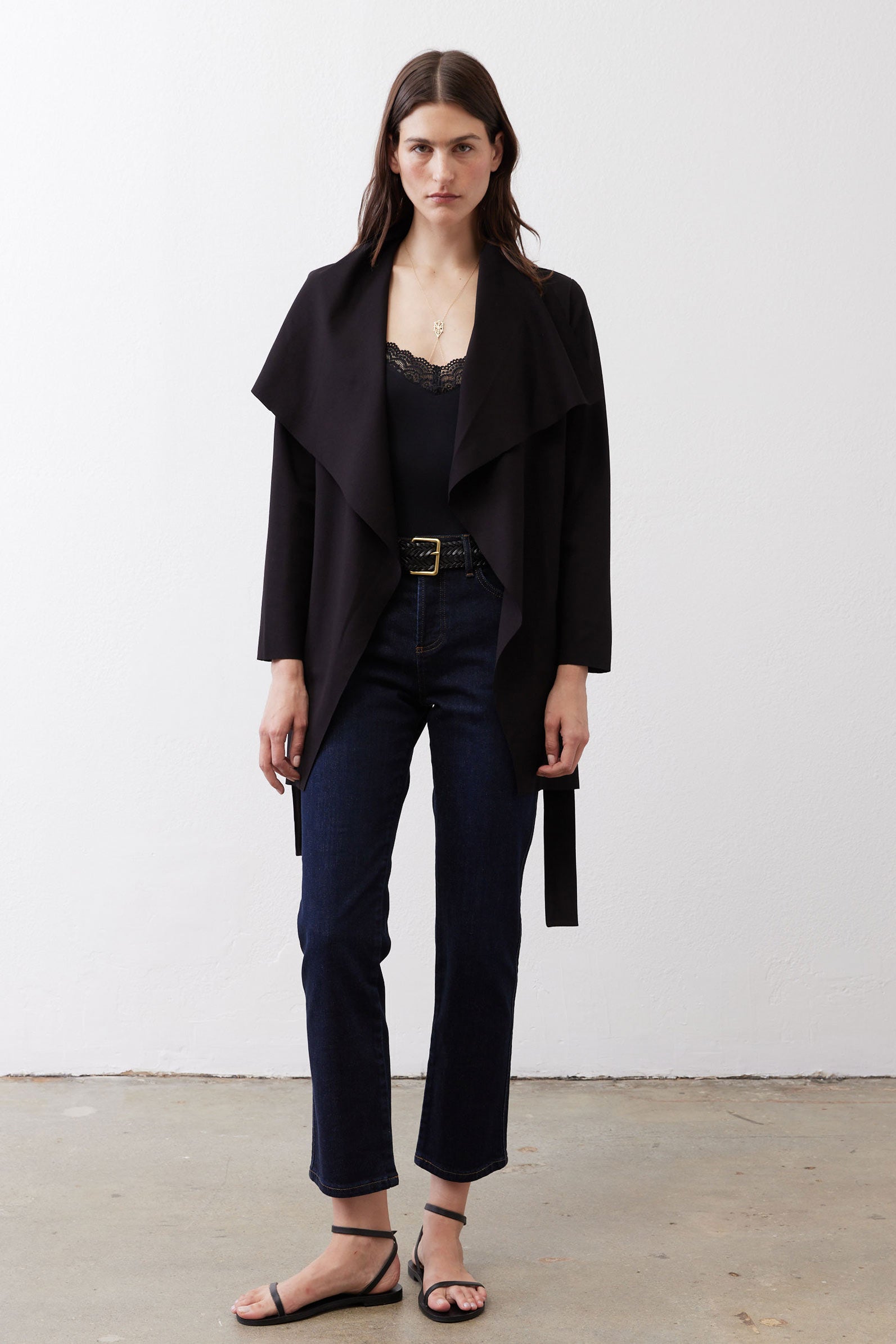 Black draped jacket with tie belt over dark jeans, open front.