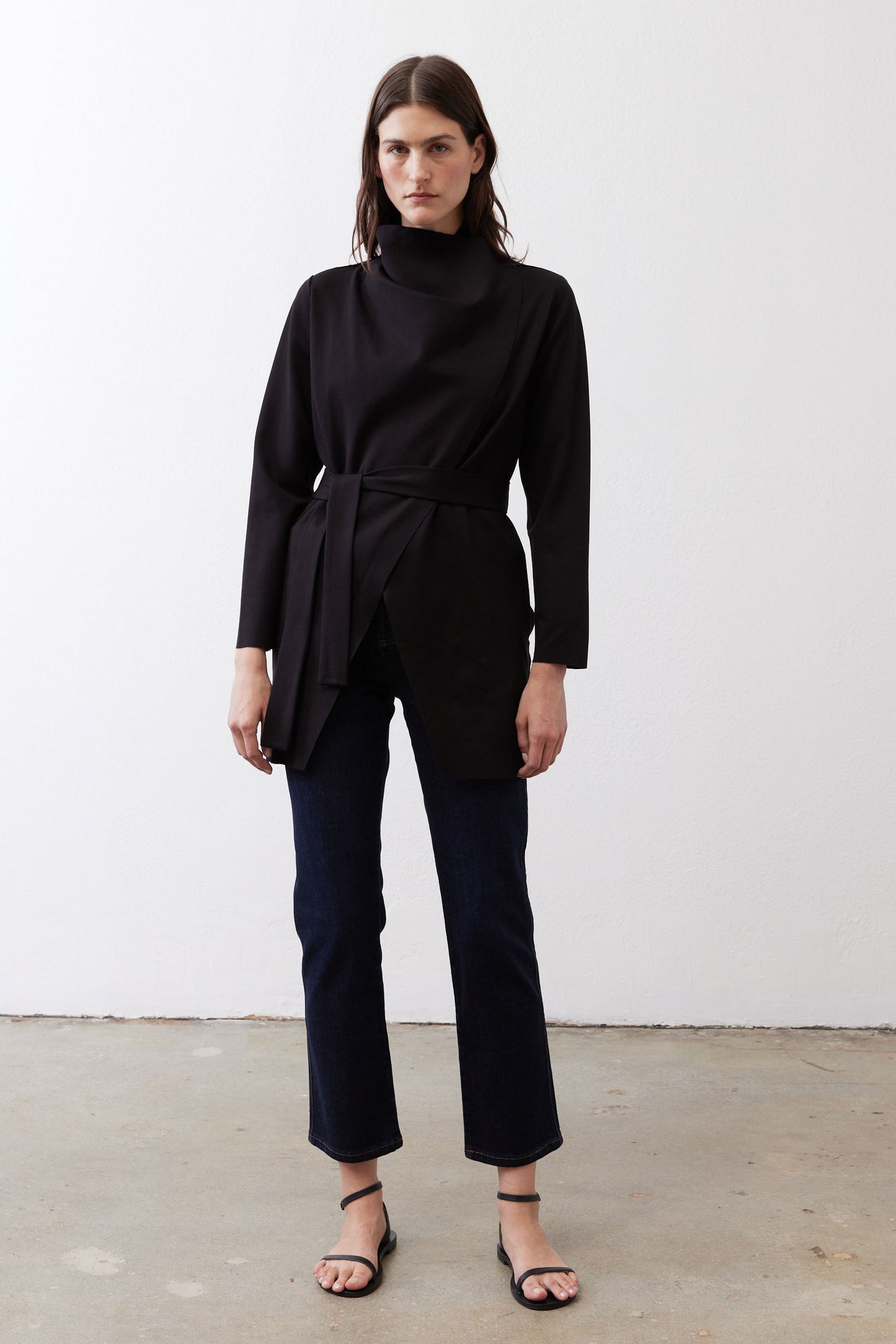 Black belted jacket with high neckline, long sleeves, and asymmetrical drape.