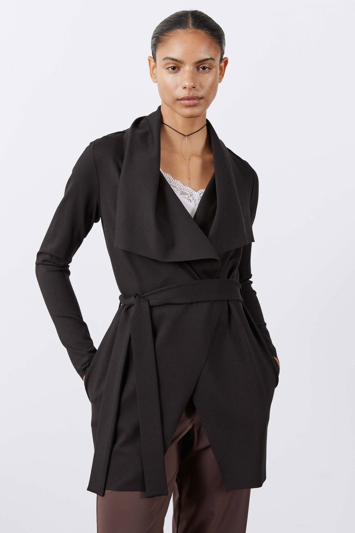 Black wrap-style draped jacket with waist belt, long sleeves, asymmetrical hem