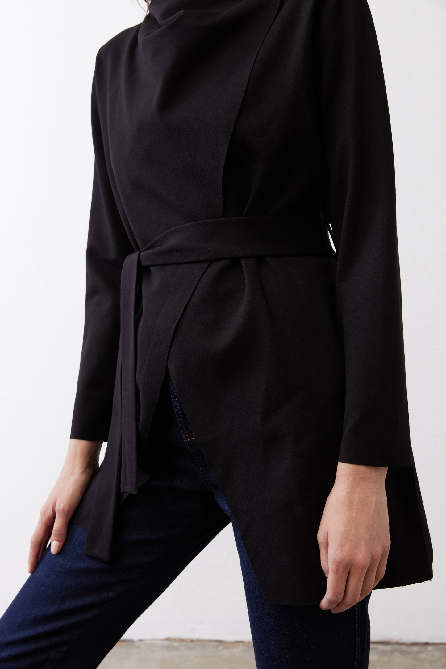 Black jacket close-up: tied waist belt and curved drape at hem.