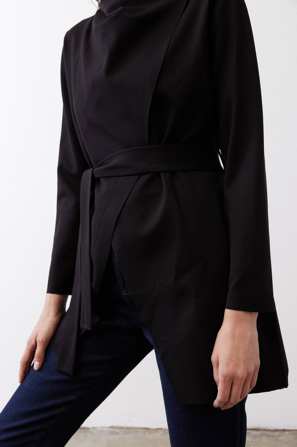 Black longline jacket with waist tie belt and side drape over dark jeans